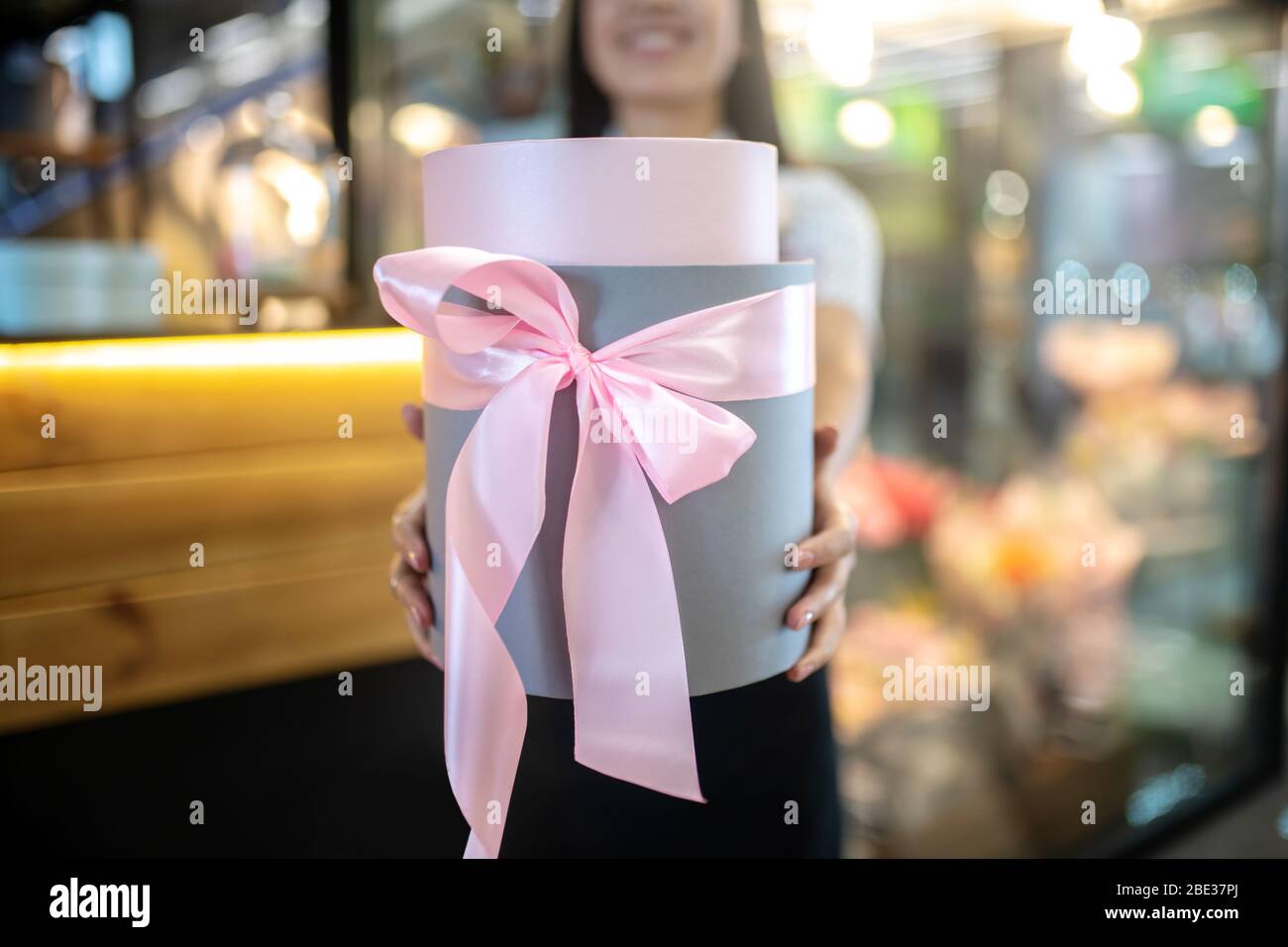 Assistente di negozio femminile dai capelli scuri che tiene una scatola regalo Foto Stock