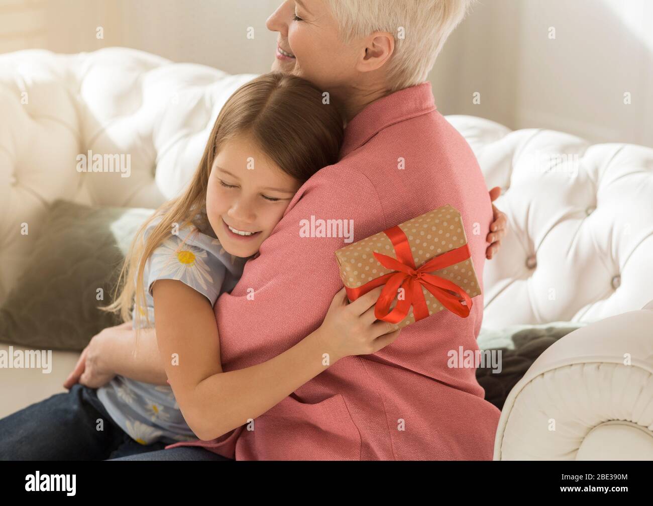 Ragazza grata con scatola regalo che abbrancano la nonna in stanza chiara Foto Stock