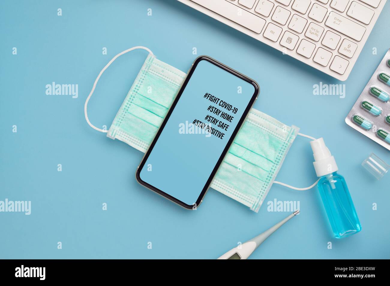 Coronavirus o Covid-19 focolaio soggiorno a casa soggiorno sicuro soggiorno concetto di backgroud positivo. Telefono cellulare con maschere facciali e alcool mano sprey su TA blu Foto Stock