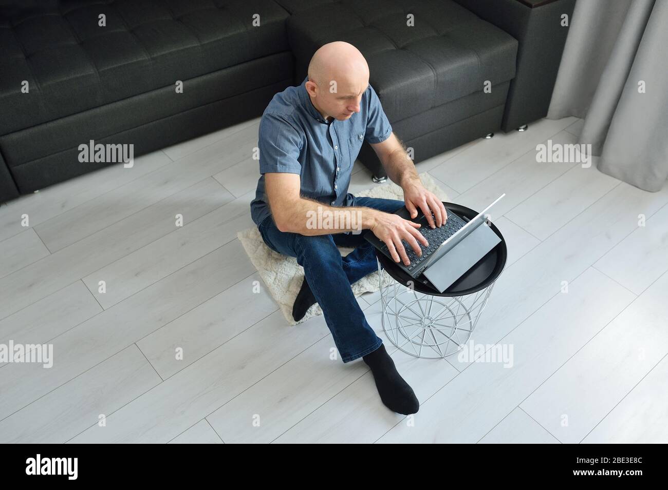 Giovane uomo in abiti casual seduto sul pavimento e lavorando sul suo computer portatile a casa. Rimani a casa e lavora online. Concetto di quarantena Foto Stock