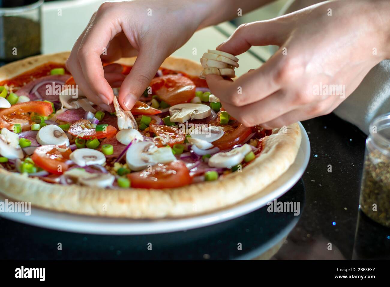 Pizza fatta in casa con verdure. Il processo di preparazione della pizza a casa. Mani di donna che fanno la pizza e che mette i funghi sulla parte superiore. Organizzazione degli ingredienti Foto Stock