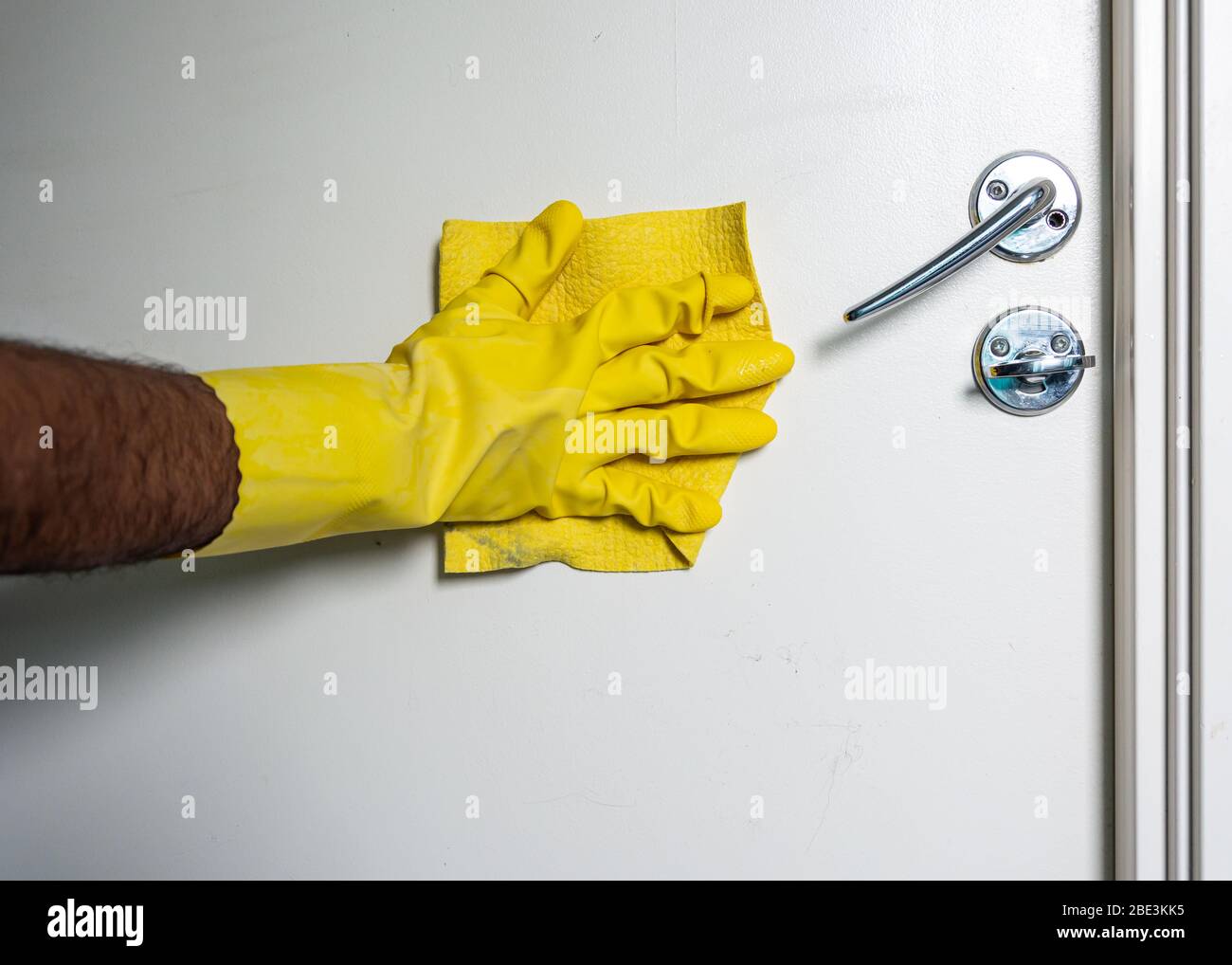 Pulizia con spray antibatterico a mano maschile indossando guanti gialli per evitare la diffusione di covid-19, Svezia Foto Stock