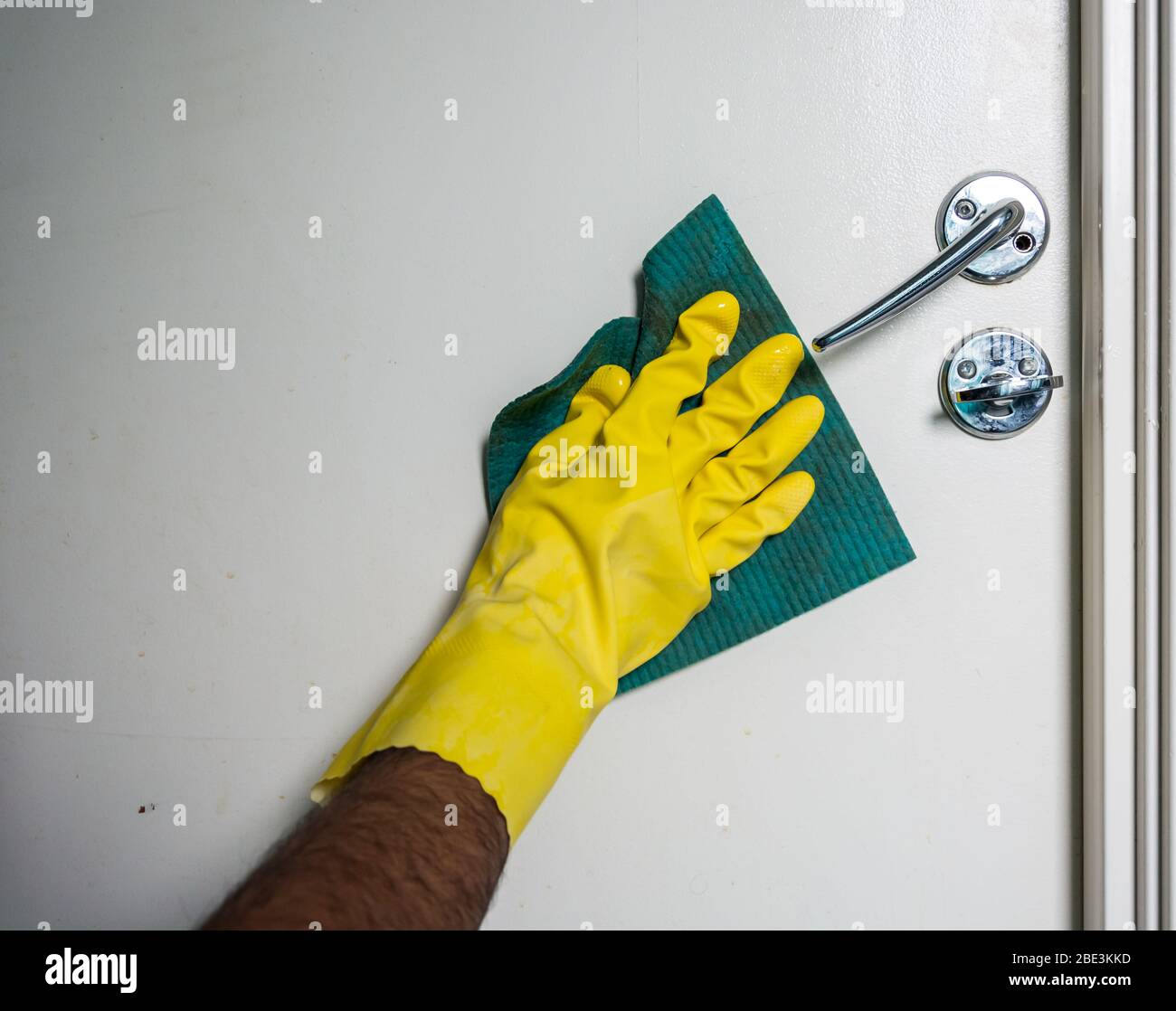 Pulizia con spray antibatterico a mano maschile indossando guanti gialli per evitare la diffusione di covid-19, Svezia Foto Stock