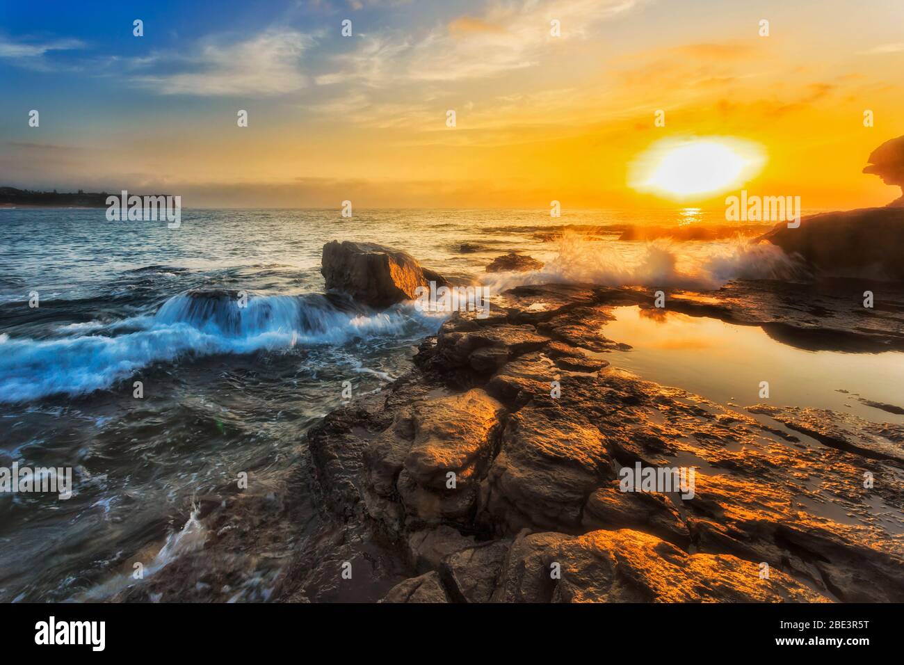 Sole sull'orizzonte dell'oceano pacifico al largo di Turimetta dirigiti verso le spiagge del nord di Sydney con onde che rotolano su rocce di arenaria. Foto Stock