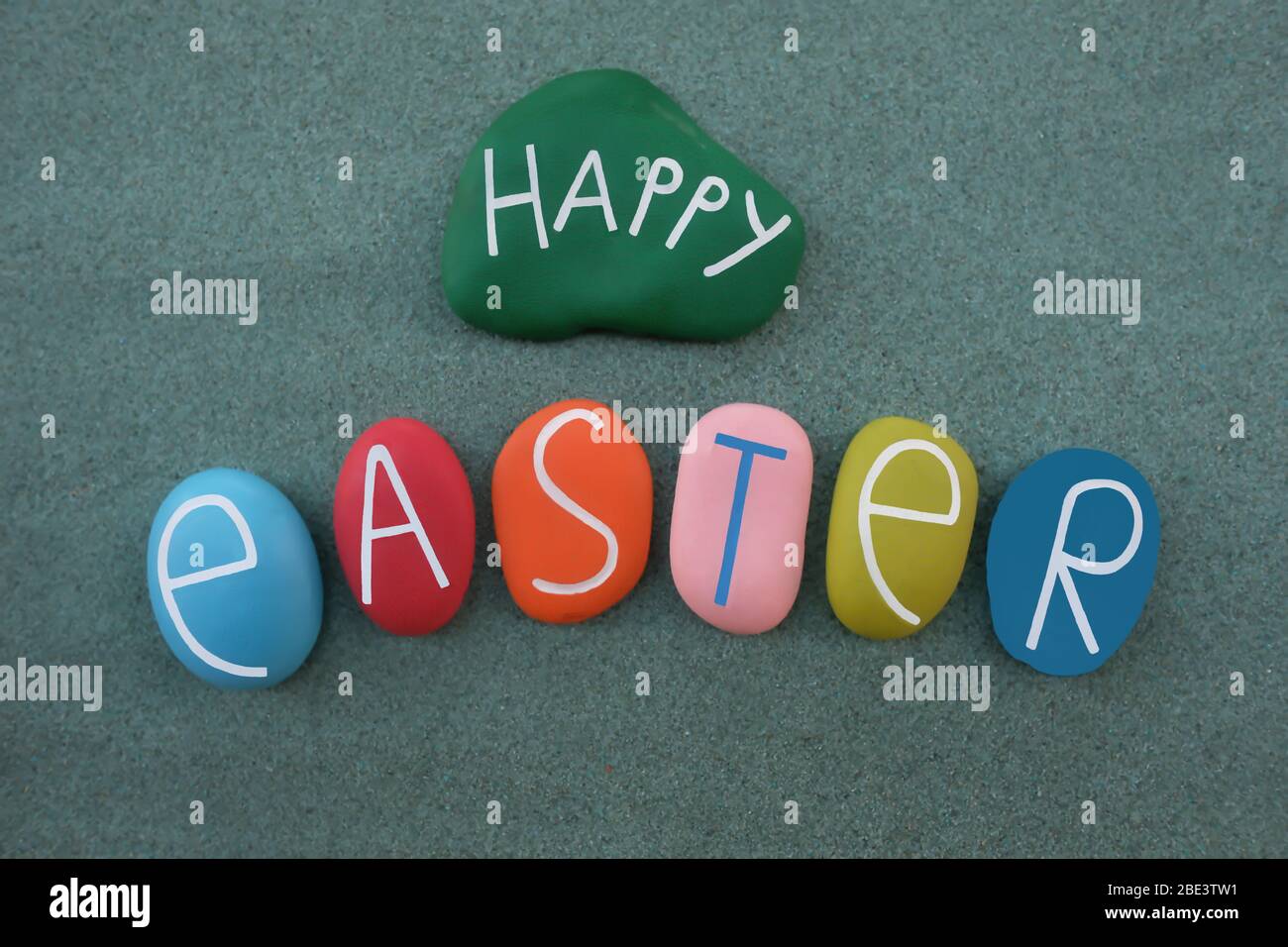 Buona Pasqua con pietre dipinte a mano colorate su sabbia verde Foto Stock