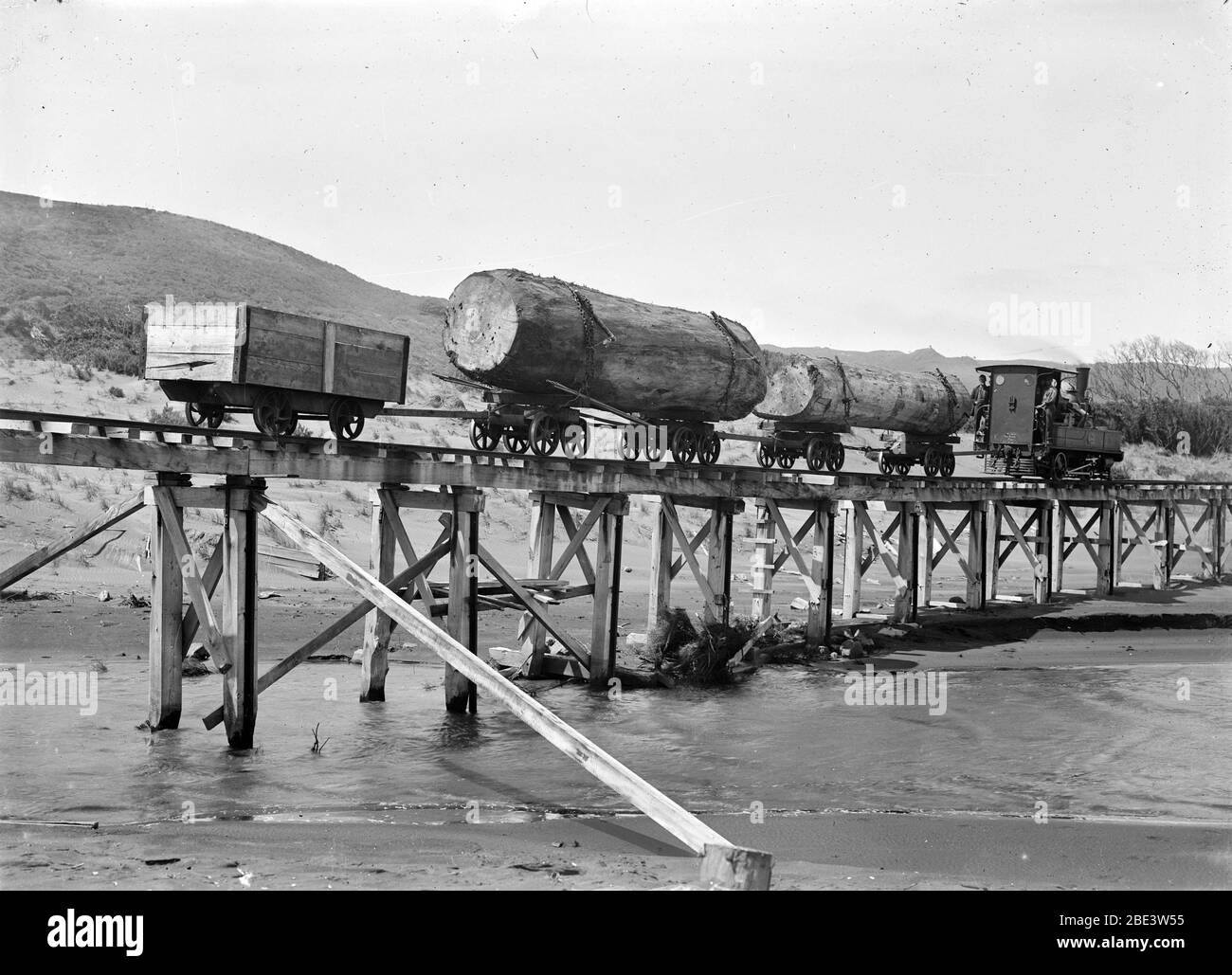 Una locomotiva traina kauri tronchi attraverso Maori Creek vicino Piha nel Nord Isola della Nuova Zelanda, circa 1915, dal fotografo Albert Percy Godber Foto Stock