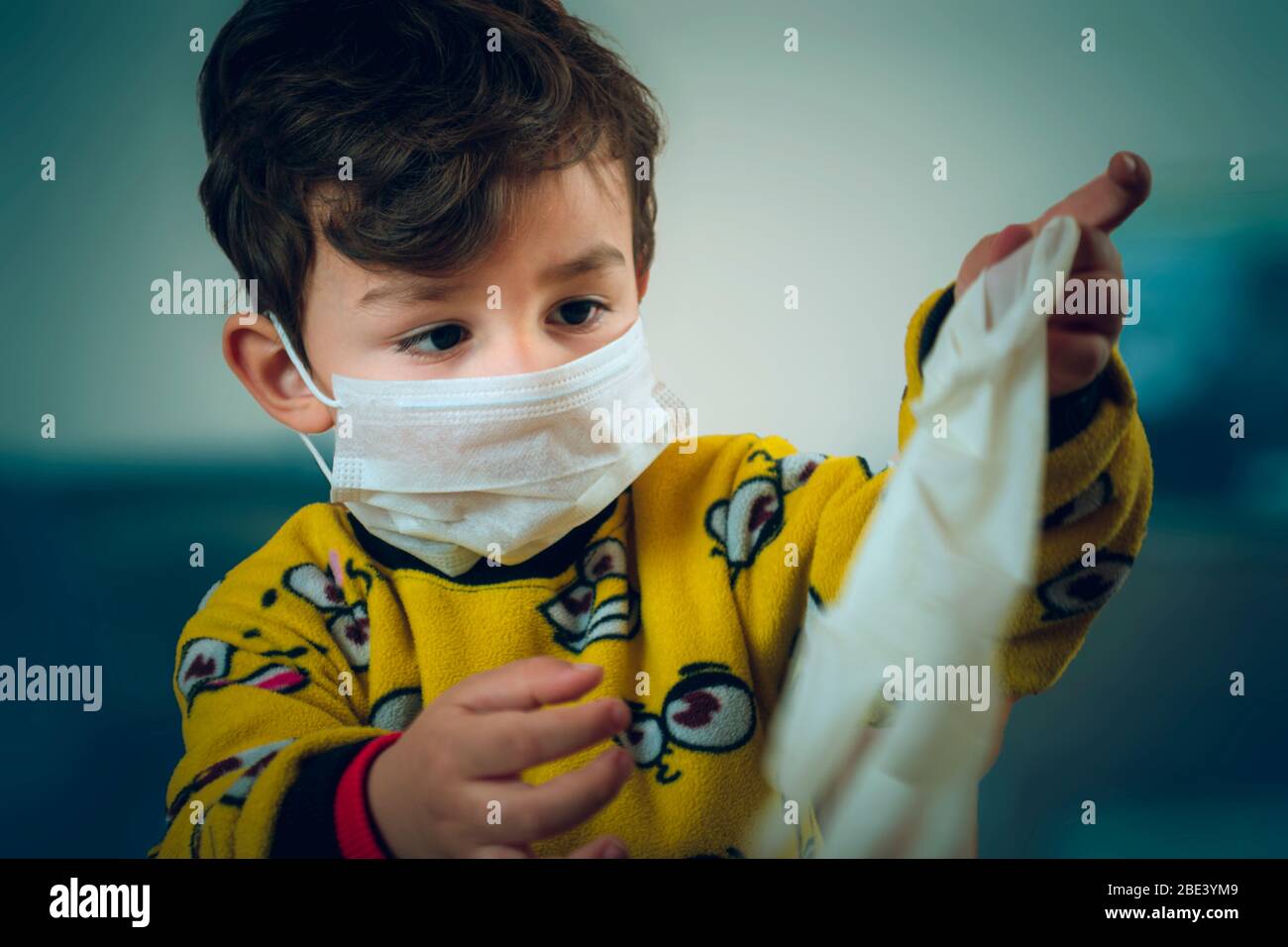 Felice guardando 3 anni bambino turco che indossa pigiama e maschera gioca con guanti chirurgici Foto Stock