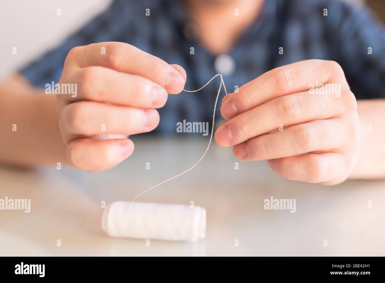 Giovane uomo che infilano un filo bianco in un ago. Processo di realizzazione di una maschera protettiva fatta in casa, per prevenire la diffusione del coronavirus, Covid-19 Foto Stock