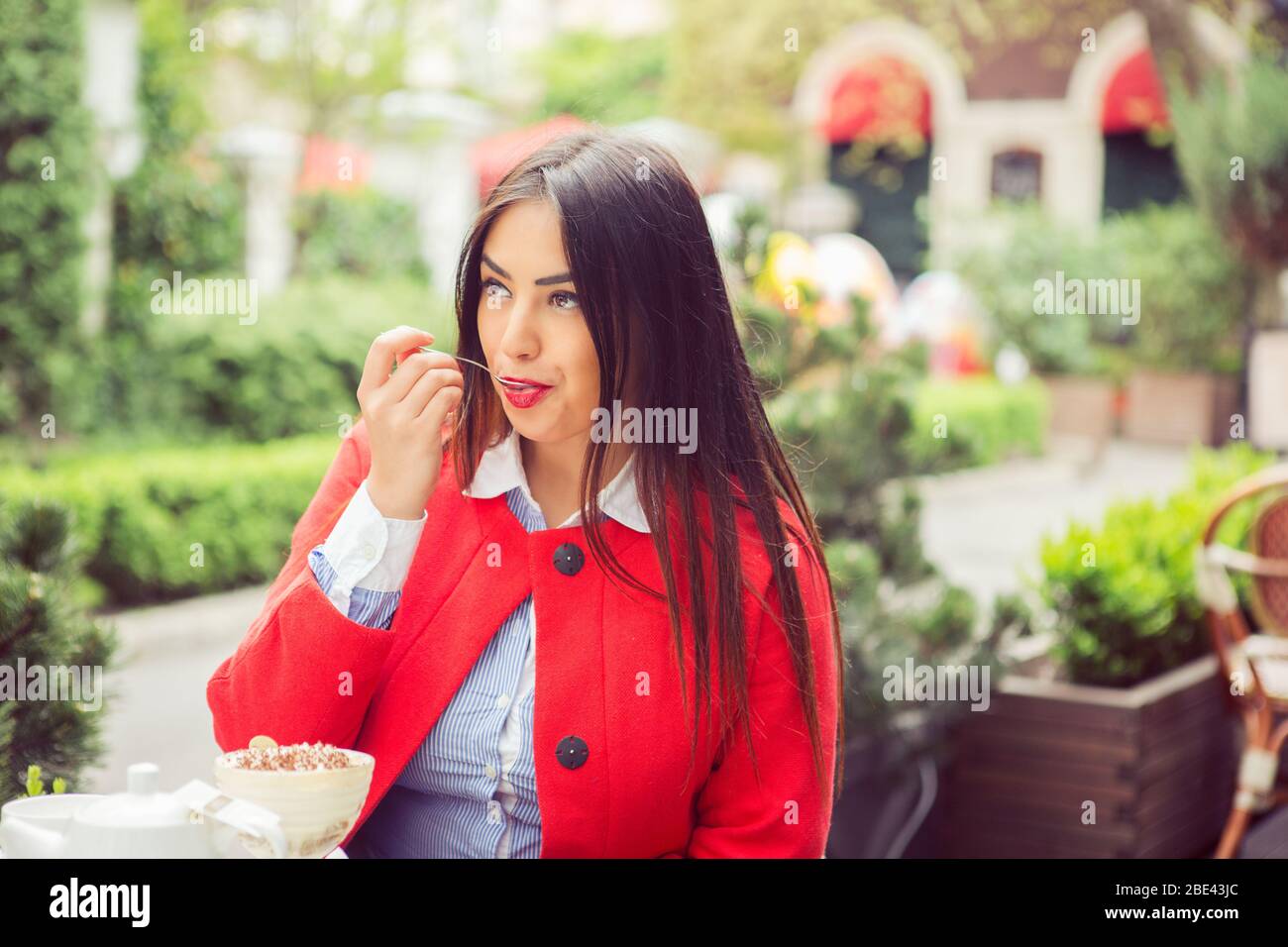 Primo piano ritratto di una giovane donna che mangia gelato lecca cucchiaio all'aperto in terrazza caffè estate. Vista laterale Foto Stock