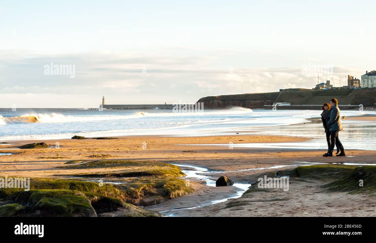 Vista panoramica di coppia a piedi sul British Seaside al tramonto a Tynemouth, Regno Unito Foto Stock