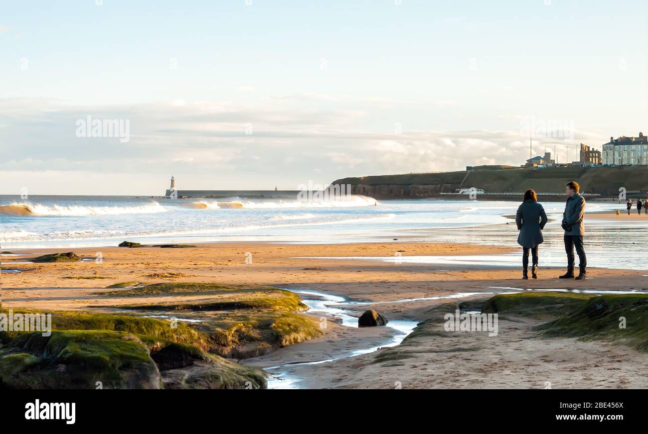 Vista panoramica di coppia a piedi sul British Seaside al tramonto a Tynemouth, Regno Unito Foto Stock