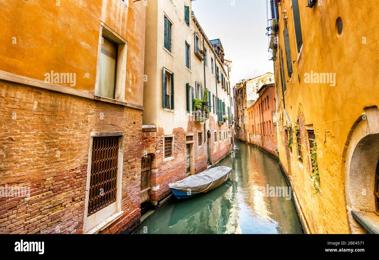 Tranquillo canale giallo veneziano con barca in acqua ferma tra le case tradizionali, Venezia, Italia Foto Stock