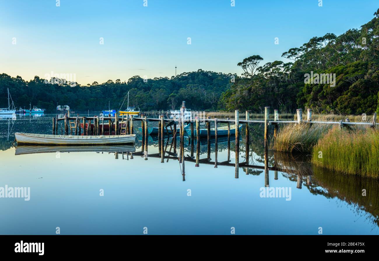 Tradizionali barche in legno ormeggiate ad un molo di legno sul Porto di Macquarie con la città di Strahan attraverso la baia sullo sfondo. Foto Stock