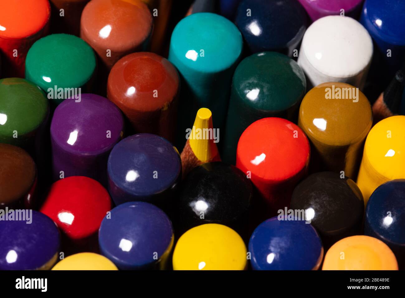 Immagine macro di un set di matite colorate dell'artista in una tazza strettamente raggruppate con le spalle rivolte verso l'alto con una punta di matita gialla che si accoppa dal centro A. Foto Stock