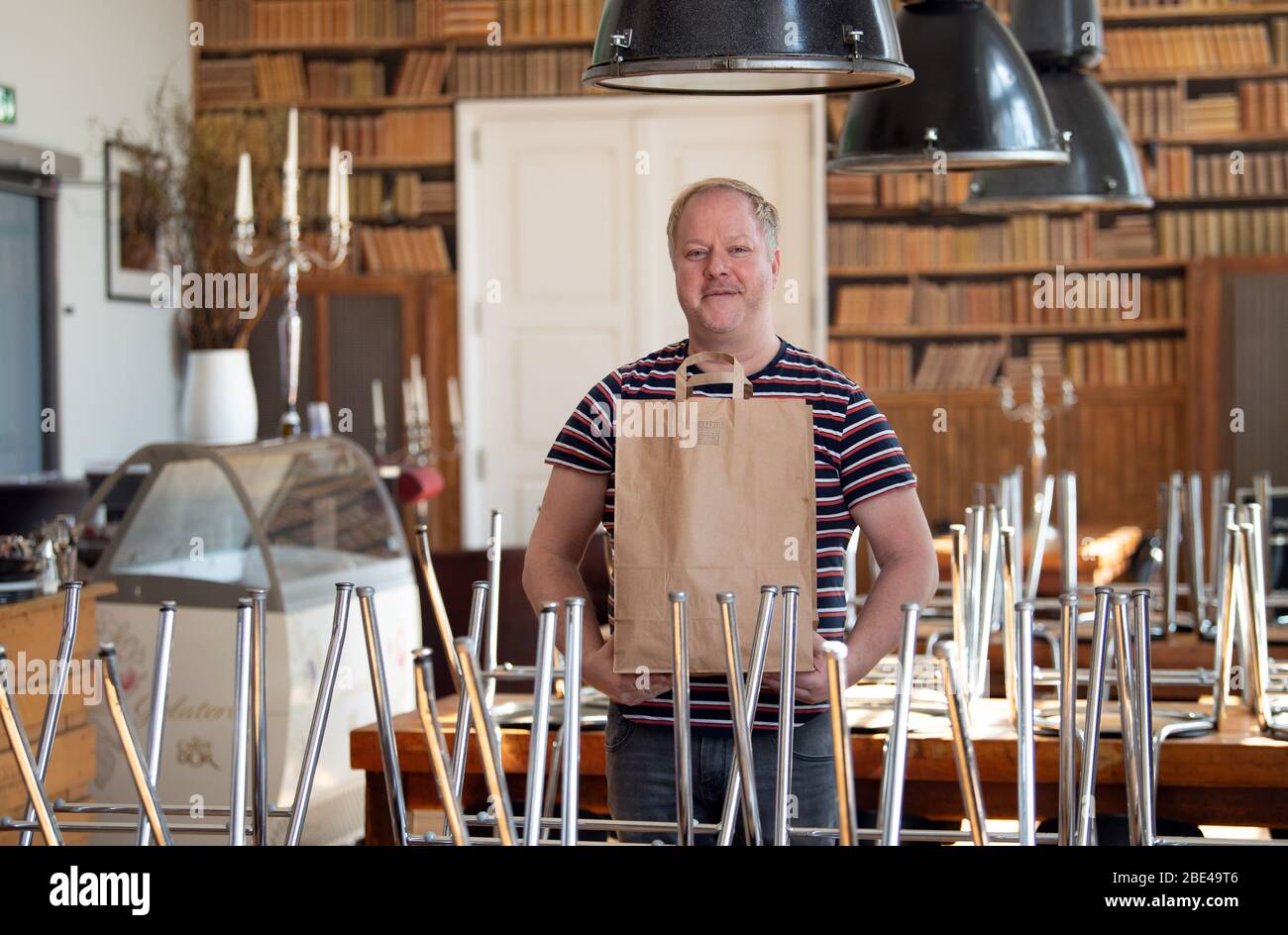 Potsdam, Germania. 07 aprile 2020. Il responsabile del servizio Conrad si trova nel ristorante "Genusswerkstatt" del Filmmuseum tra le sedie a sdraio e tiene in mano un sacchetto di carta con scatole per cibo. Non è consentito sedersi nei ristoranti durante le restrizioni imposte dal pericolo di Corona. (Per 'Cool drinks and gustoso risotto: To Go in segno di Corona') credito: Soeren Stache/dpa-Zentralbild/ZB/dpa/Alamy Live News Foto Stock