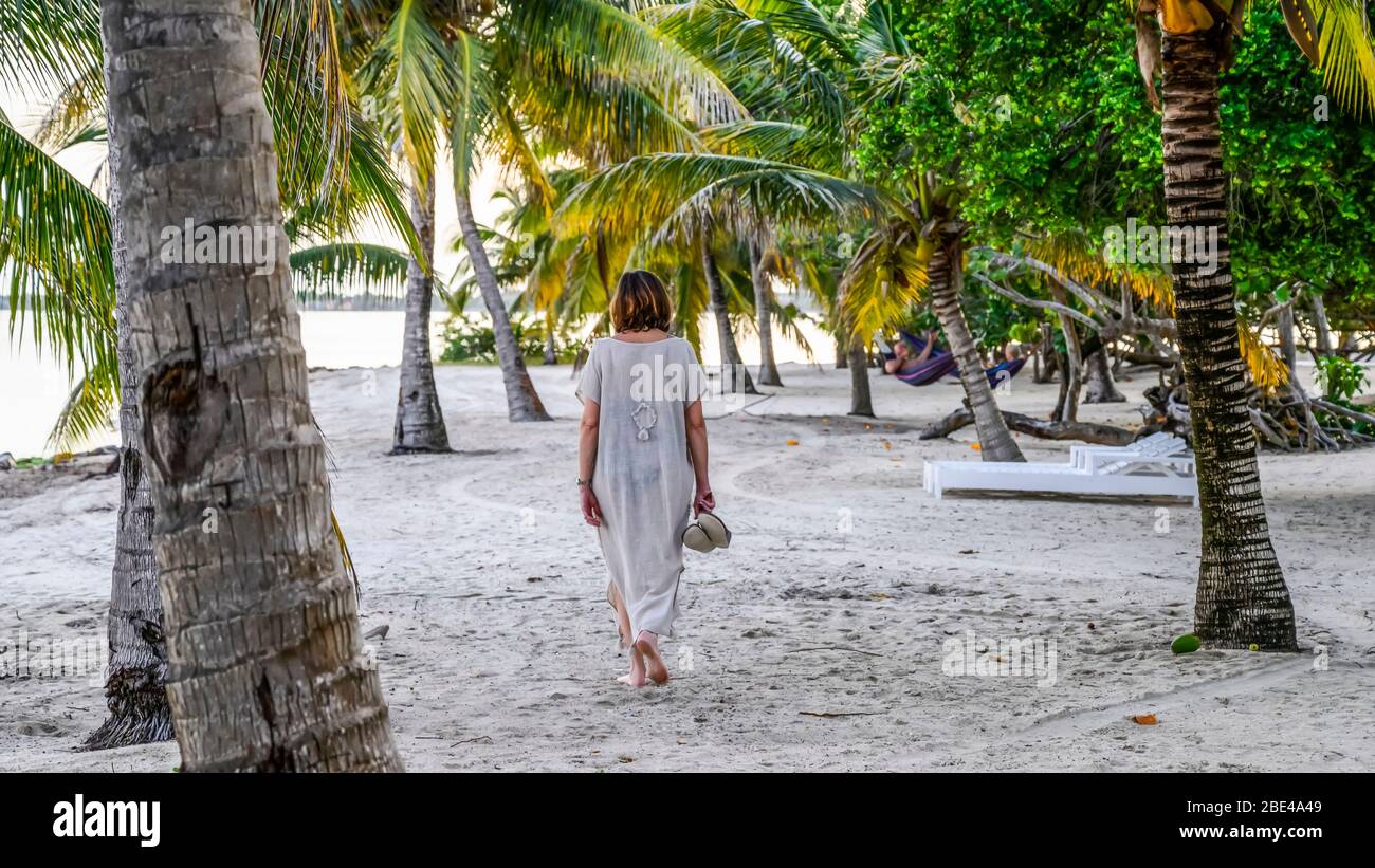 Una donna matura cammina sulla sabbia bianca tra le palme su una spiaggia dei Caraibi, Penisola di Placencia; Belize Foto Stock