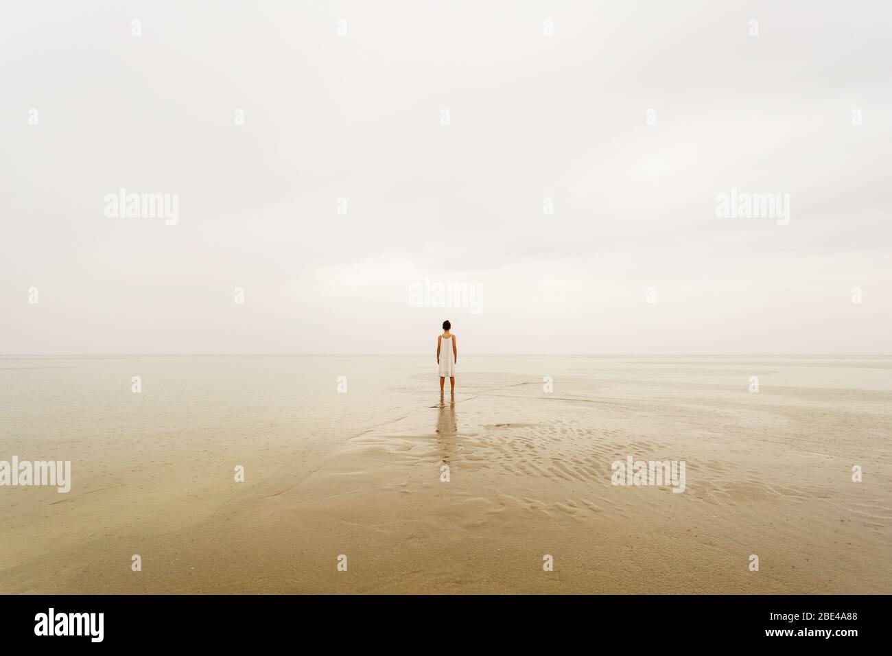 Giovane ragazza su una spiaggia sotto la pioggia che guarda lontano dalla macchina fotografica. Sfondo ispirato con spazio di copia ideale per la quotazione Foto Stock