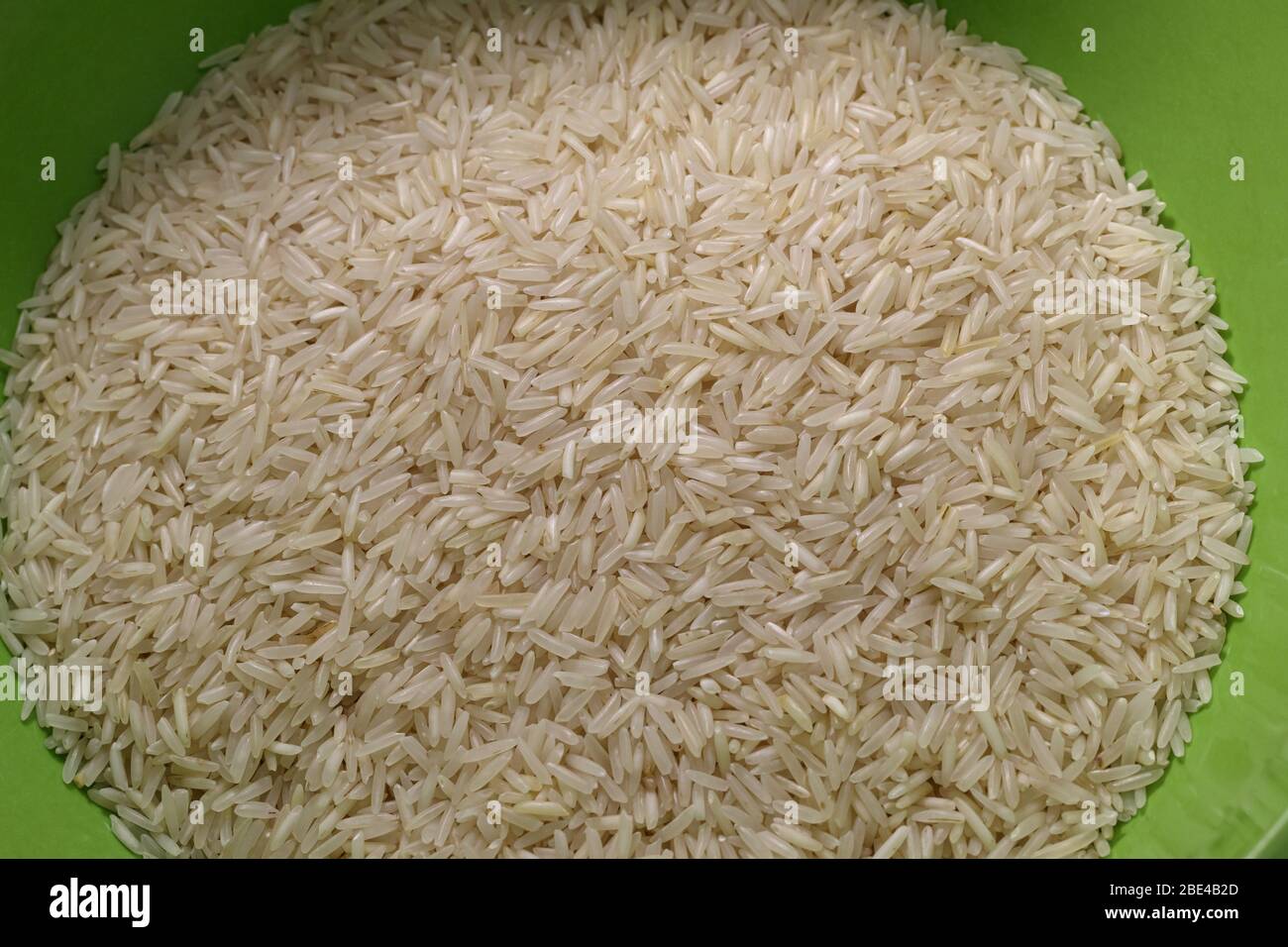 Una ciotola verde di riso basmati bianco secco è visibile dall'alto, mostrando il dettaglio dei grani. Foto Stock