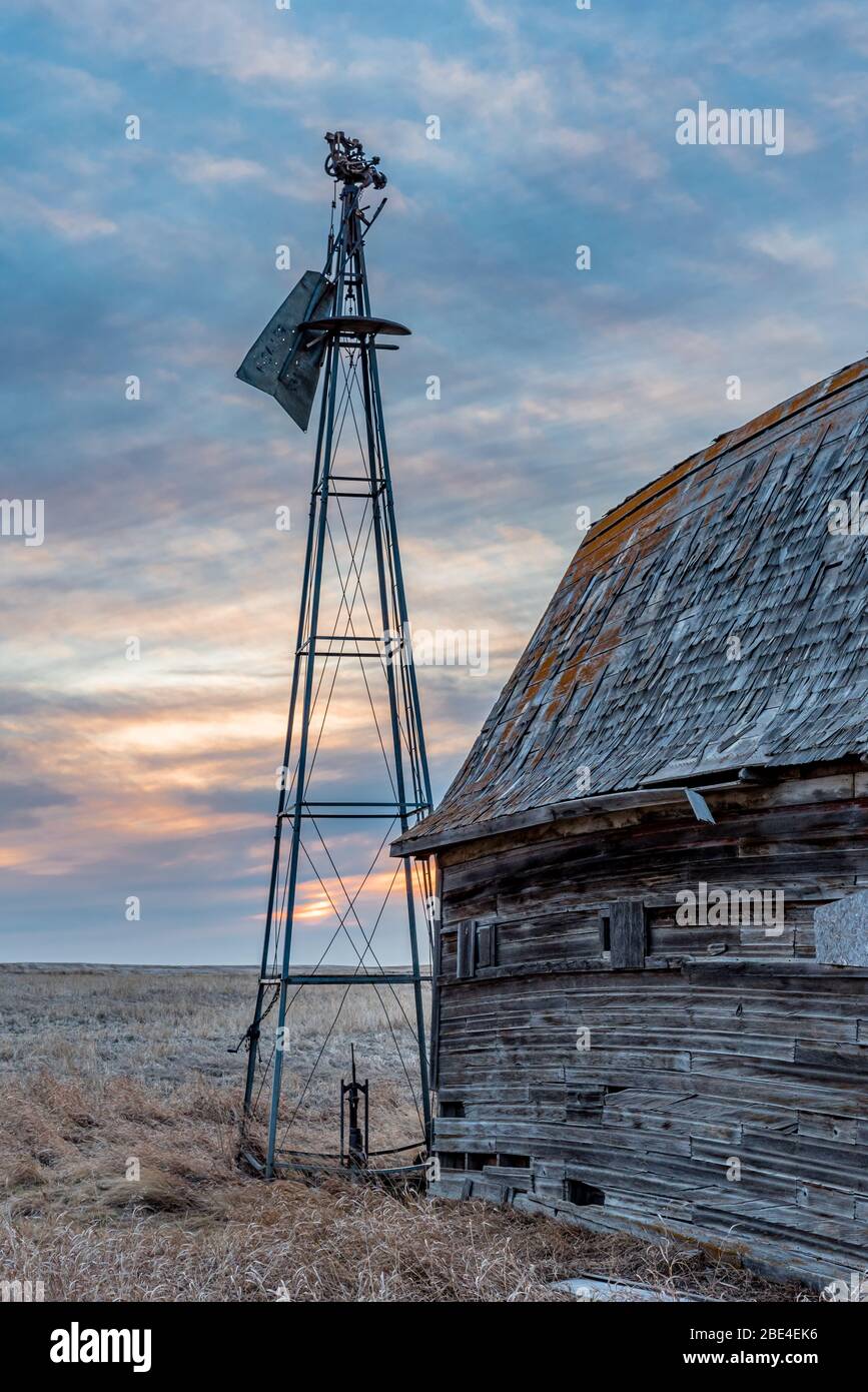 Tramonto su un mulino a vento vintage rotto accanto ad un vecchio fienile sulle praterie in Saskatchewan Foto Stock