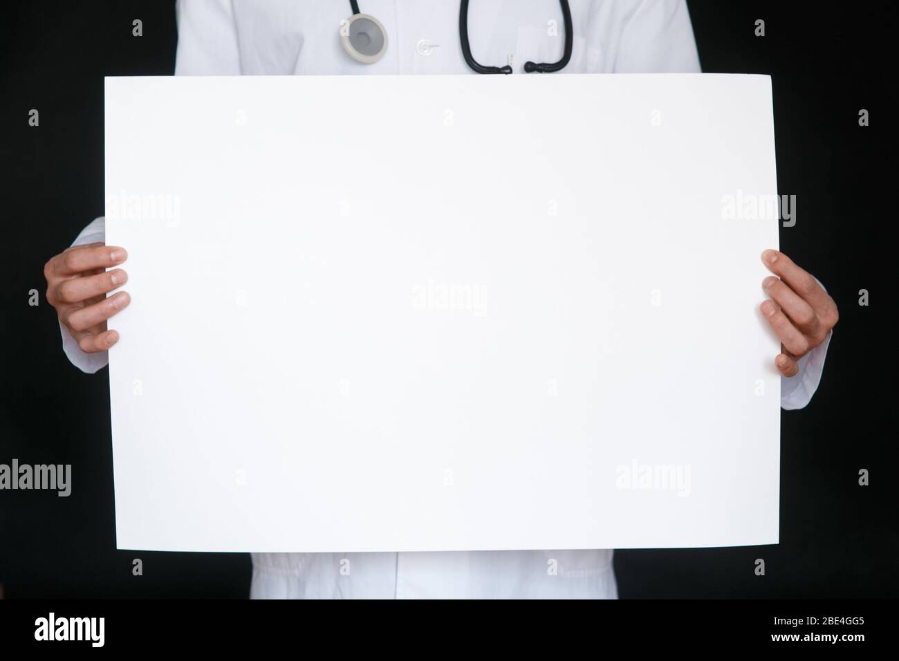 Un uomo in una t-shirt nera e guanti medici tiene un foglio bianco di carta. Mockup. Coronavirus. Quarantena . Epidemia. Spazio di copia. Avvertenza. Mano del medico in guanto blu che tiene fogli di carta. Foto Stock