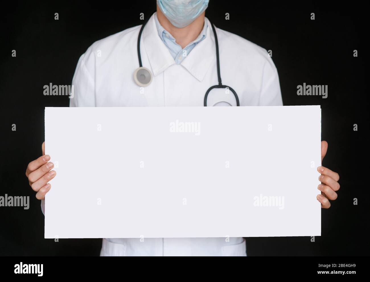 Un uomo in una t-shirt nera e guanti medici tiene un foglio bianco di carta. Mockup. Coronavirus. Quarantena . Epidemia. Spazio di copia. Avvertenza. Mano del medico in guanto blu che tiene fogli di carta. Foto Stock