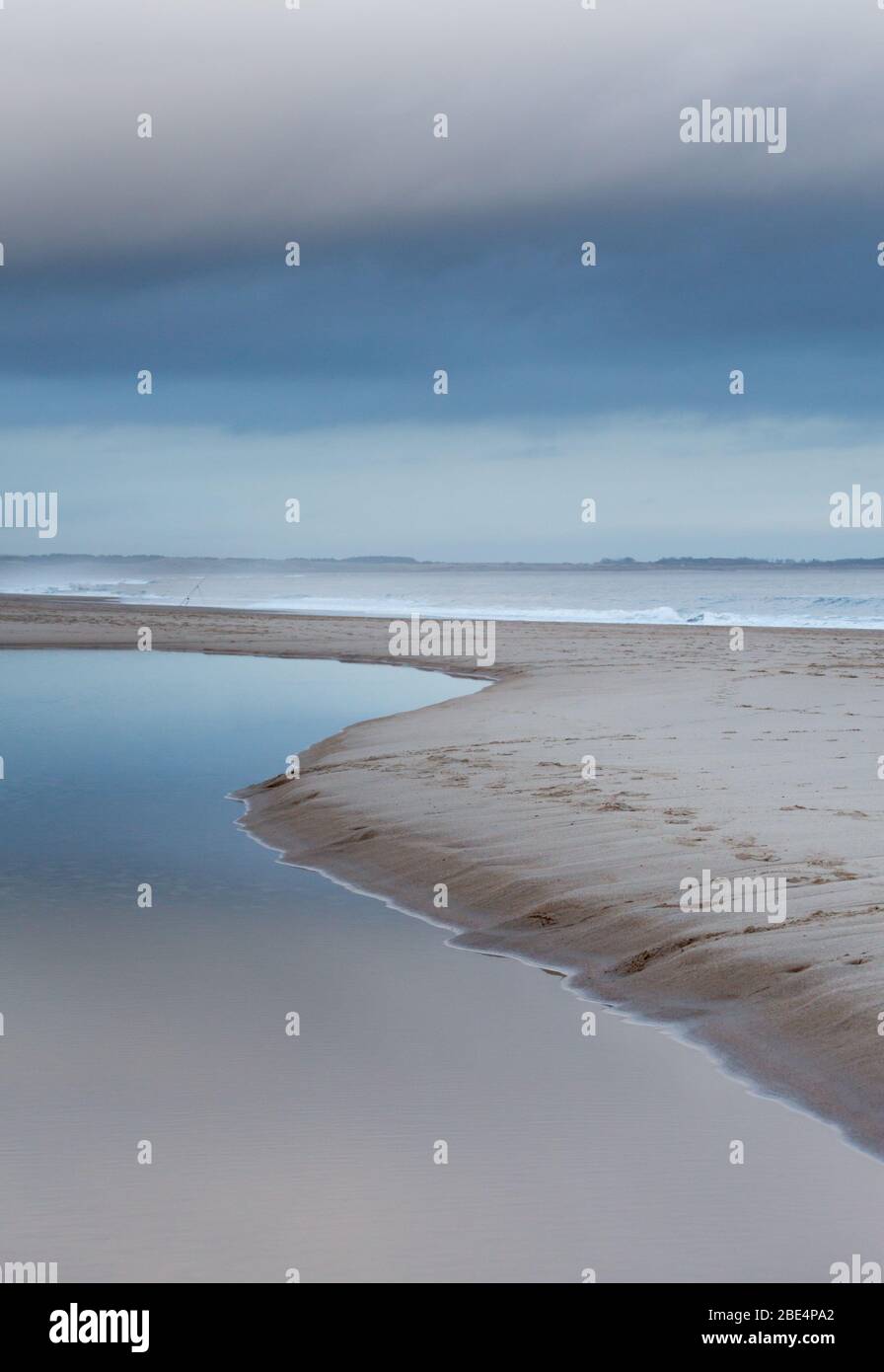La linea curva di un ruscello che attraversa la sabbia e conduce al mare a Drumidge Bay, Northumberland, nel nord-est dell'Inghilterra. Foto Stock