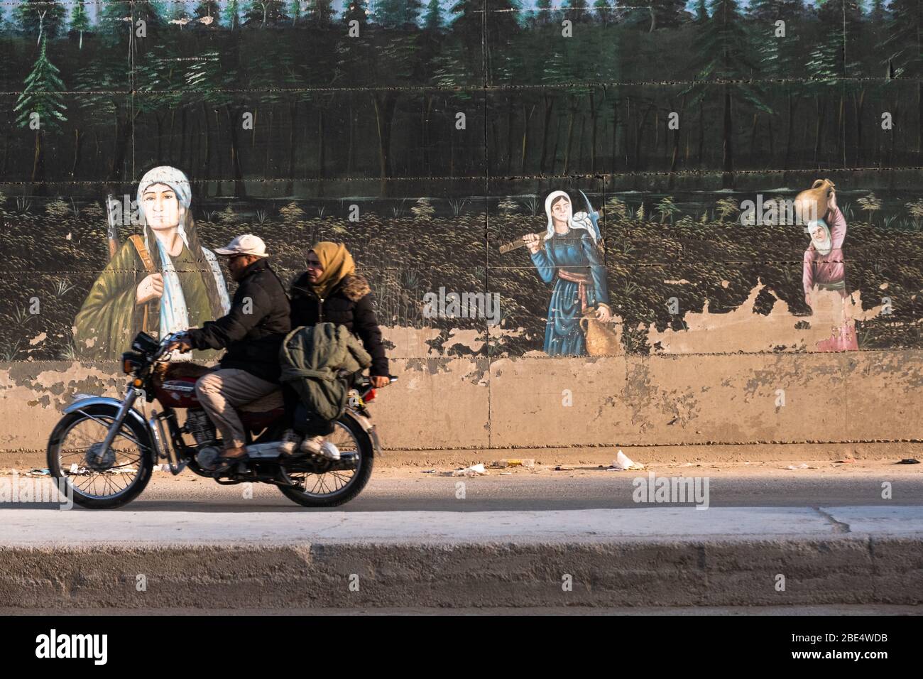 Un paio di cavalcate davanti a un murale che raffigura la lotta dei lavoratori a Qamishli, in Siria. Foto Stock
