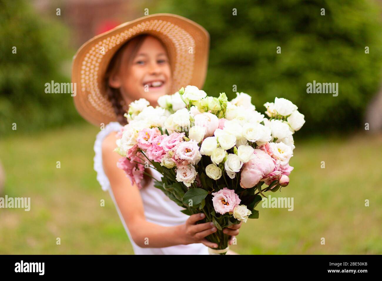 Una ragazza sorridente tiene in mano un bel bouquet di peonie rosa e bianca. Un bambino in un cappello di paglia. Giornata estiva soleggiata. Foto Stock