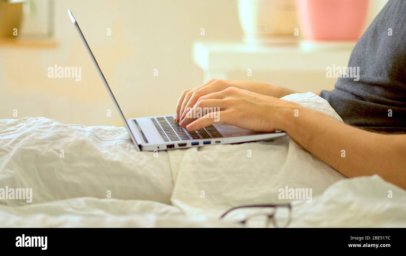 Un uomo lavora in camera da letto presso un computer portatile. Telelavaggio a casa durante il periodo di quarantena del coronavirus Covid 19. Foto Stock