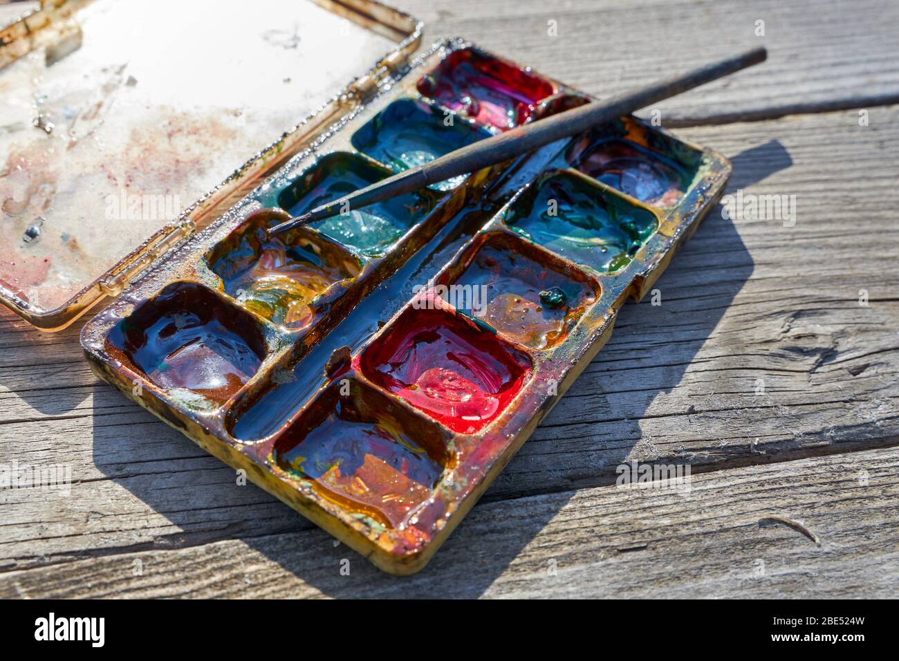 Palette di vecchie pitture miste con un pennello giace su un vecchio tavolo di legno grigio Foto Stock