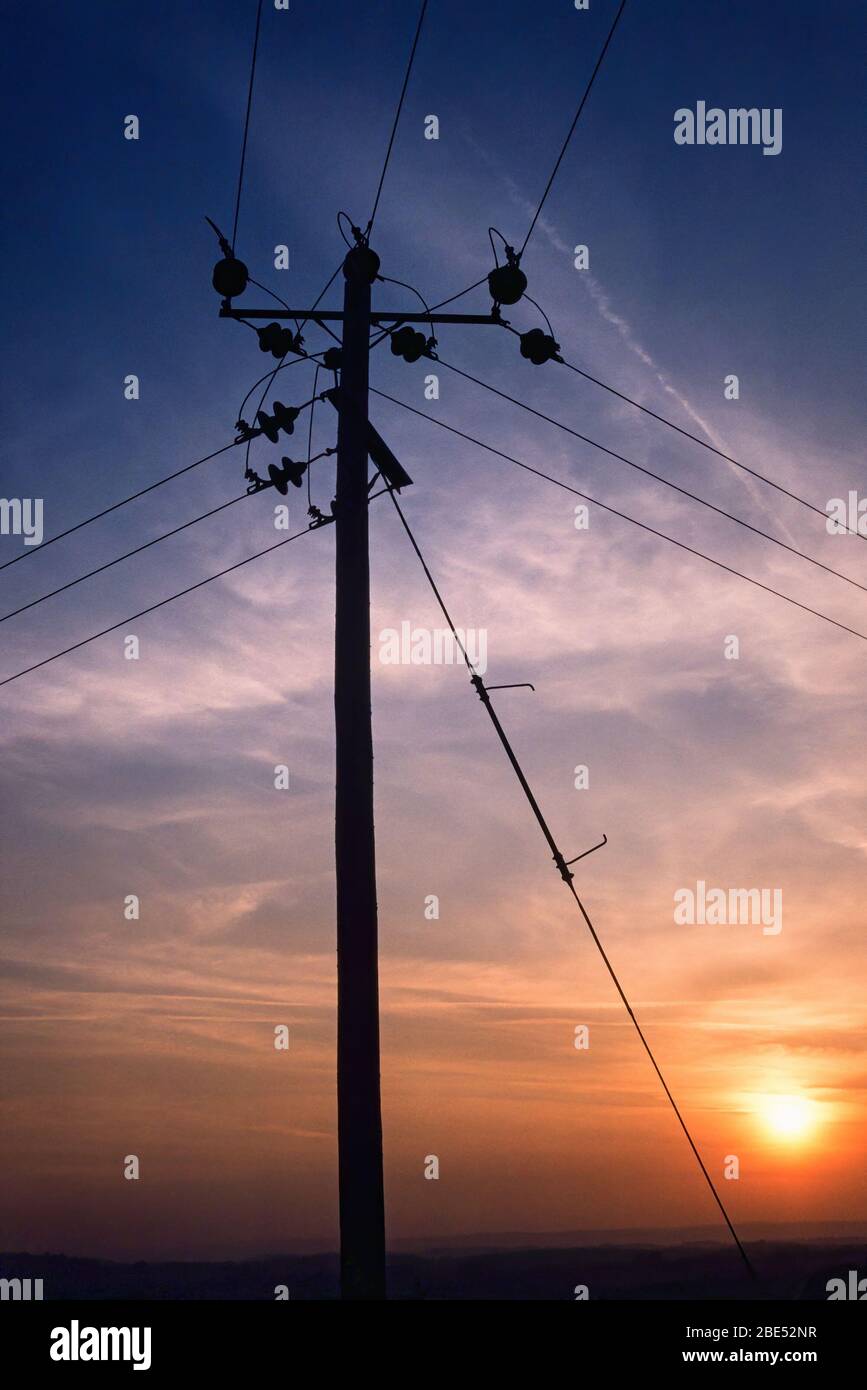 Palo di distribuzione elettrica in legno e cavi in silhouette contro un cielo tramonto sera, Inghilterra, Regno Unito Foto Stock