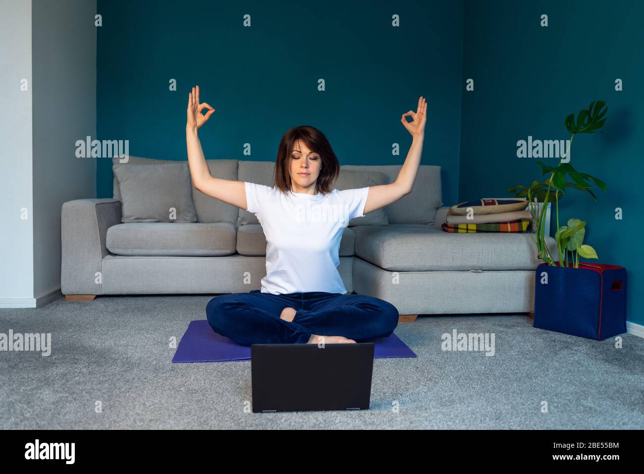 La donna sta facendo yoga online con il laptop durante l'isolamento del suo soggiorno, senza attrezzi da allenamento, suggerimenti per la meditazione per i principianti, rimanere a casa e mantenere un concetto sano Foto Stock