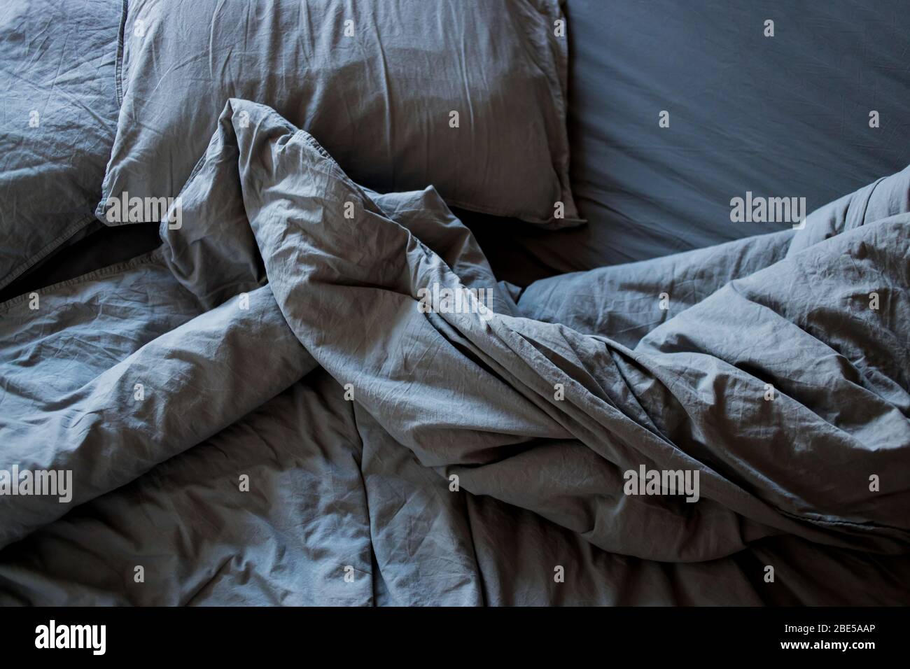 Vista superiore accartocciata letto la mattina dopo il sonno. Grigio foglio di cotone e coperte sul letto Foto Stock