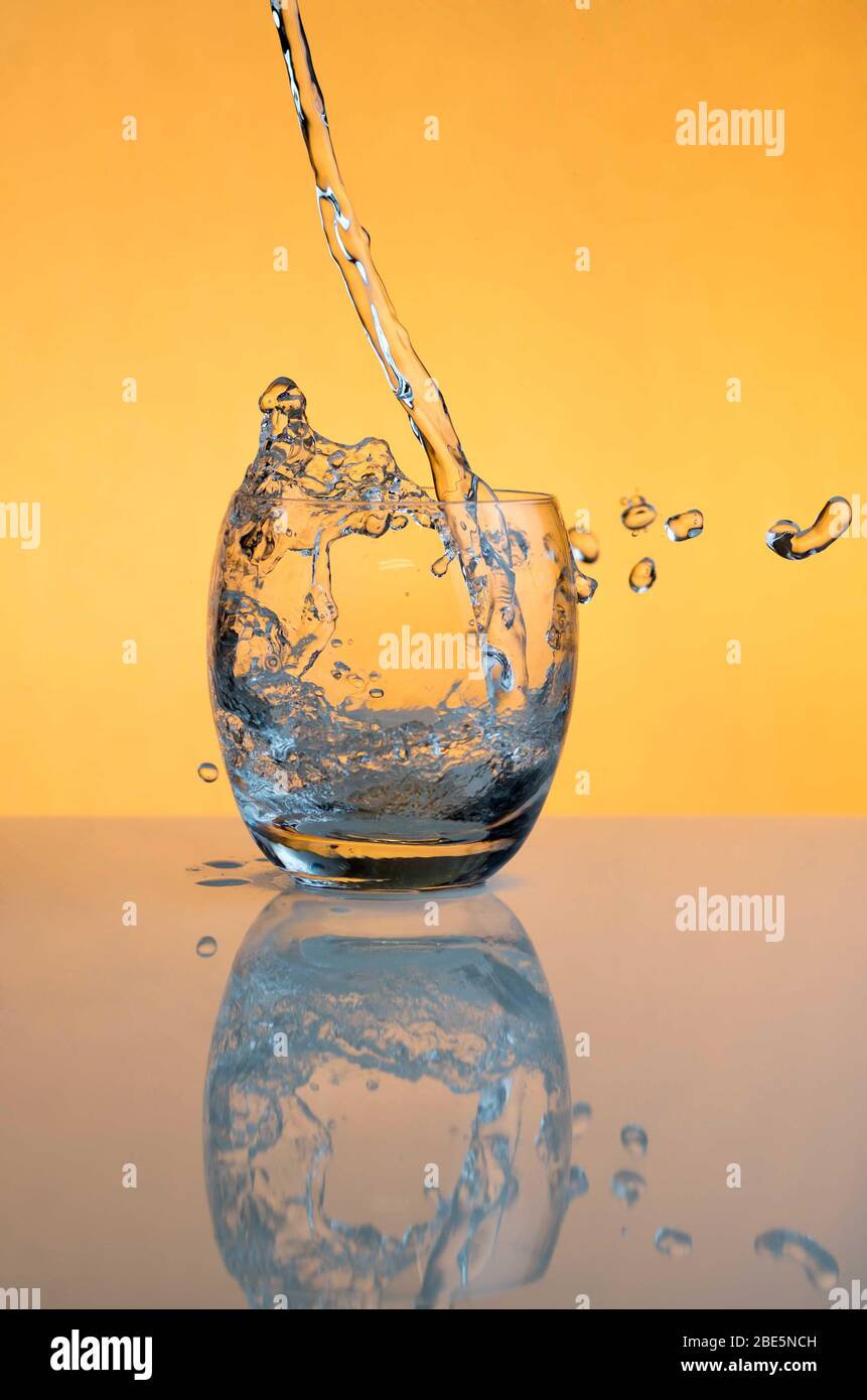 Acqua che si versa in un bicchiere e spruzzi fuori Foto Stock