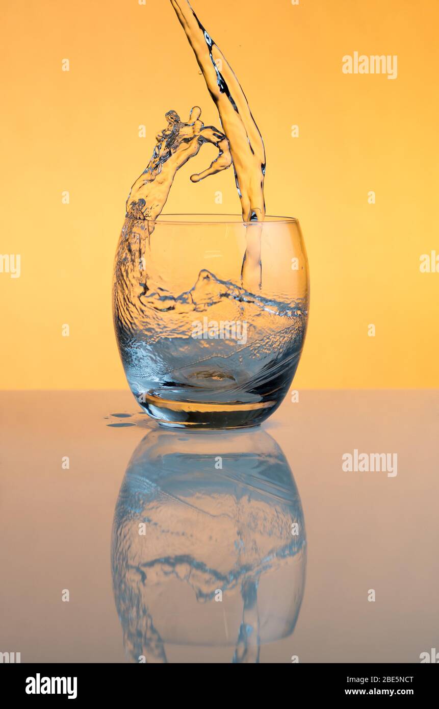 Acqua che si versa in un bicchiere e spruzzi fuori Foto Stock
