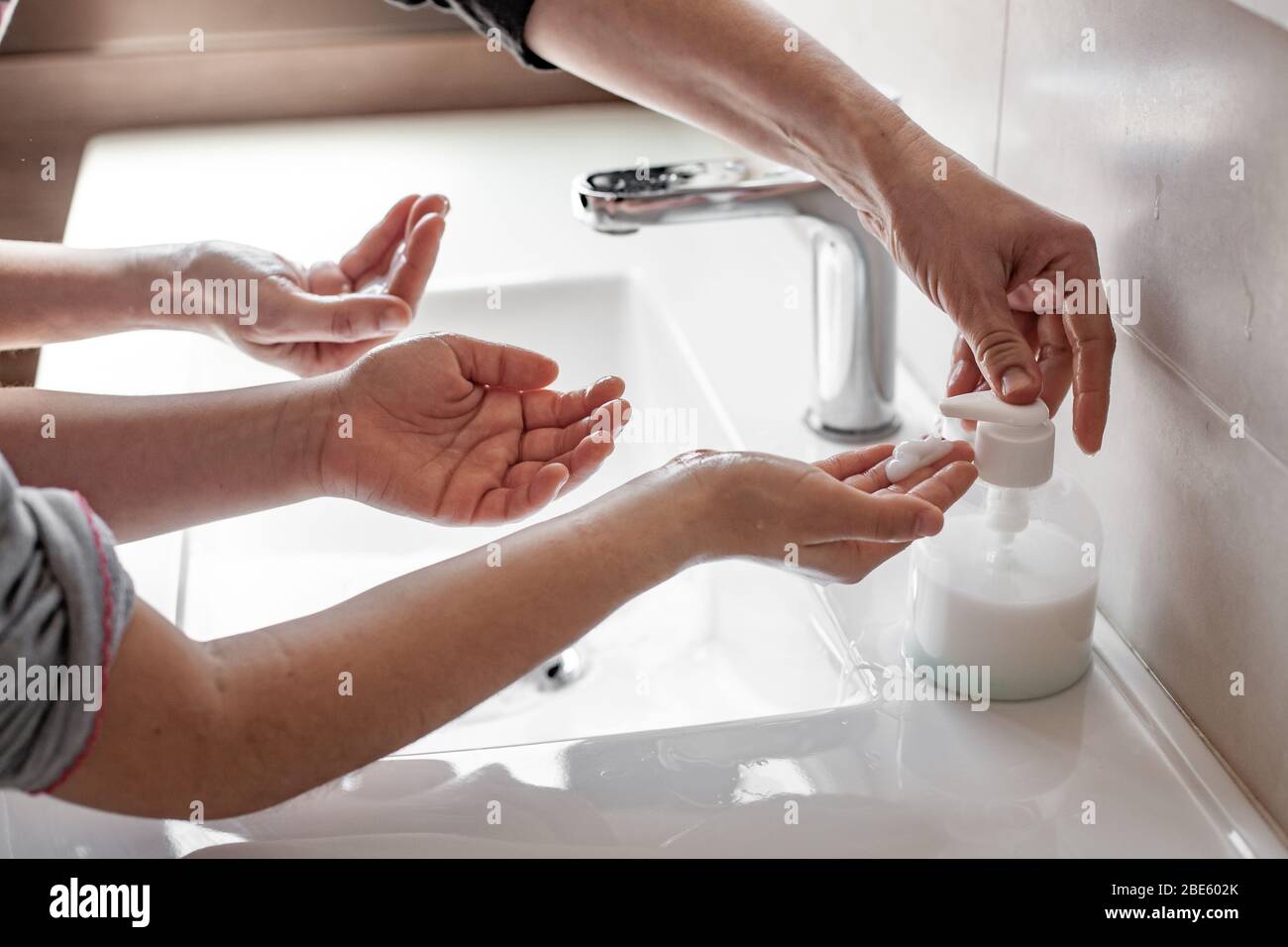 Madre che insegnava a sua figlia come lavare correttamente le loro mani con sapone per prevenire l'infezione da coronavirus Foto Stock
