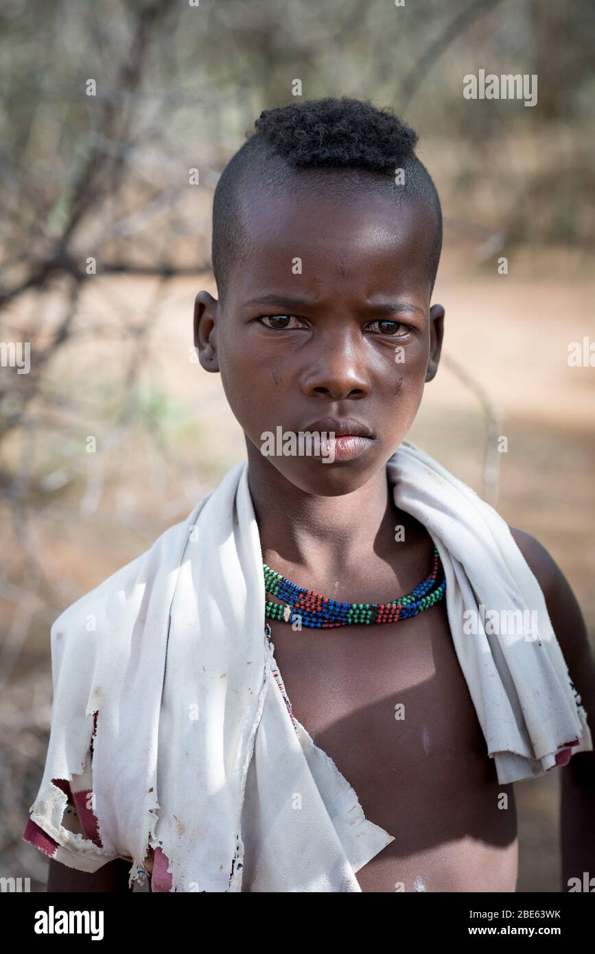 Giovane ragazzo con collana di perle è spettatore a Mursi tribù etnico gruppo venuta di età bull jumping cerimonia, Jenka, Etiopia, Foto Stock