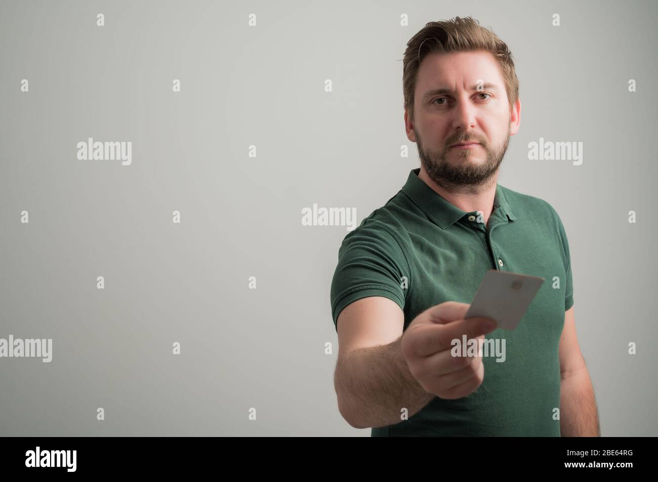 Ritratto di uomo serio elegante attraente con barba spessa, vestito in casual t shirt verde dare la carta isolata su sfondo grigio con spazio copia Foto Stock