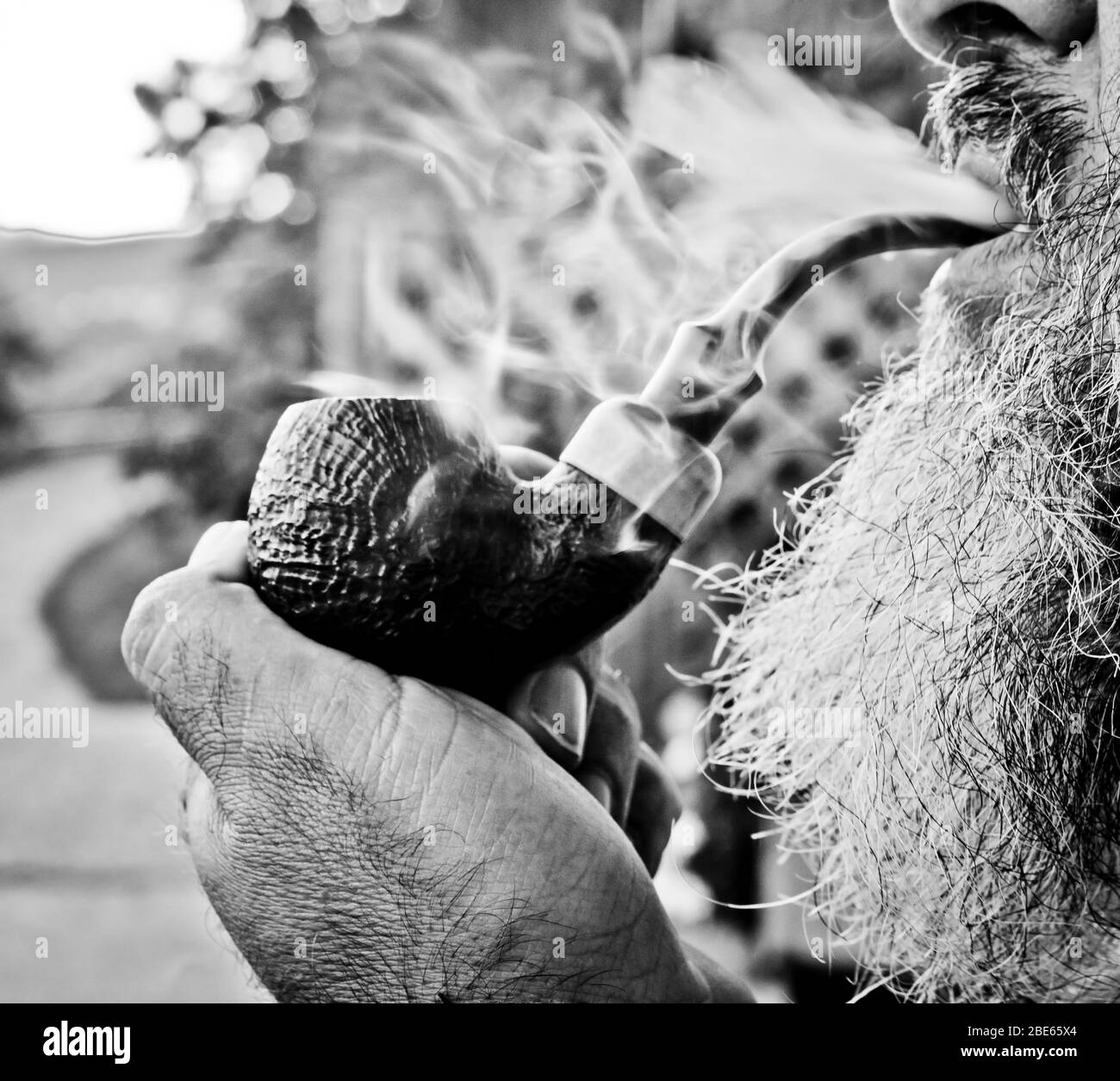 il vecchio ragazzo fuma il tabacco nella sua pipa con piacere tra dolci nuotate e nuvole di fumo Foto Stock