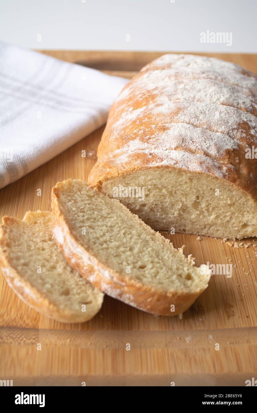 Una focaccia di pane fresco fatto in casa con farina cosparsi sopra in un asciugamano da cucina su tagliere di legno a fette Foto Stock