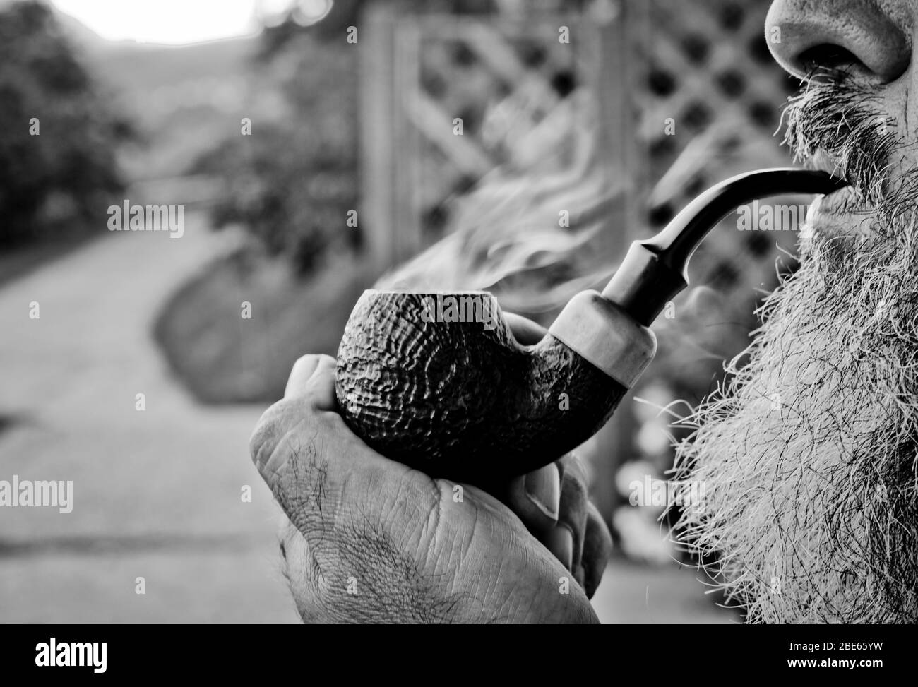 il vecchio ragazzo fuma il tabacco nella sua pipa con piacere tra dolci nuotate e nuvole di fumo Foto Stock