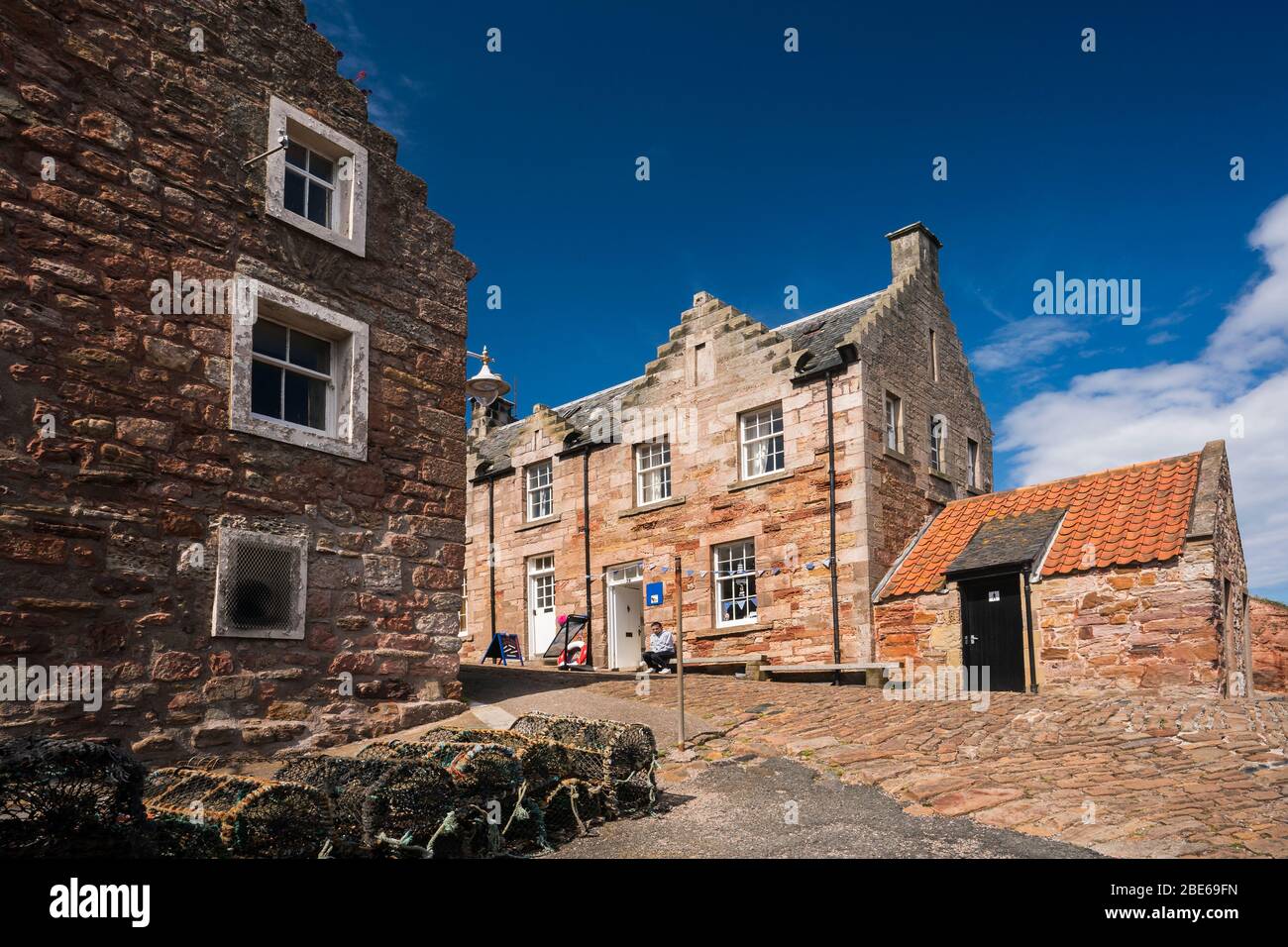 Un uomo locale siede su una panchina fuori da un edificio in pietra intorno al porto di pescatori, Crail, Regno di Fife, Scozia, Europa Foto Stock