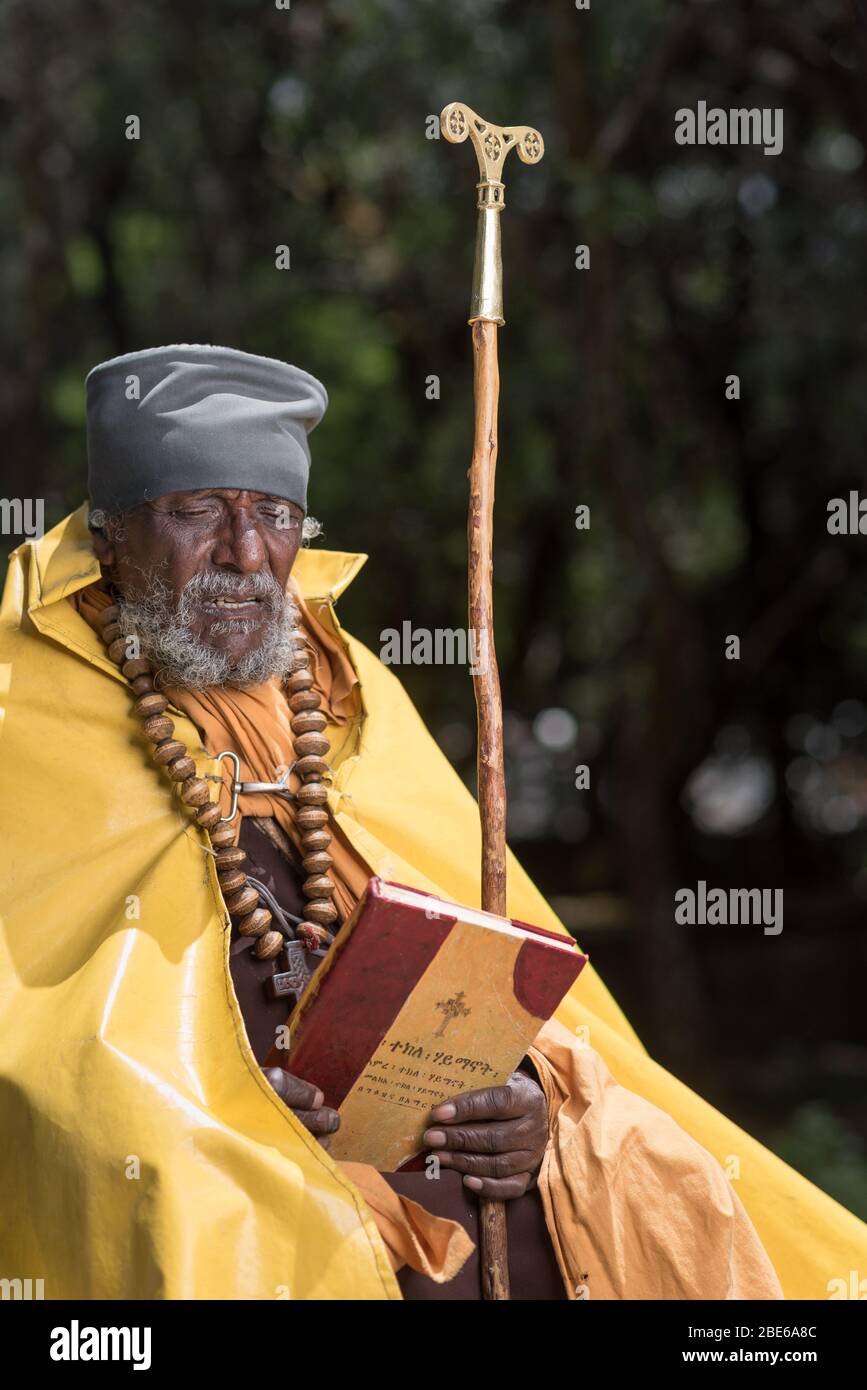 Con il suo personale e pregando con la bibbia in giardini all'aperto, un monaco etiope ortodosso della chiesa di Tewaheddo, il monastero di Debre Libanose, Etiopia, Africa. Foto Stock