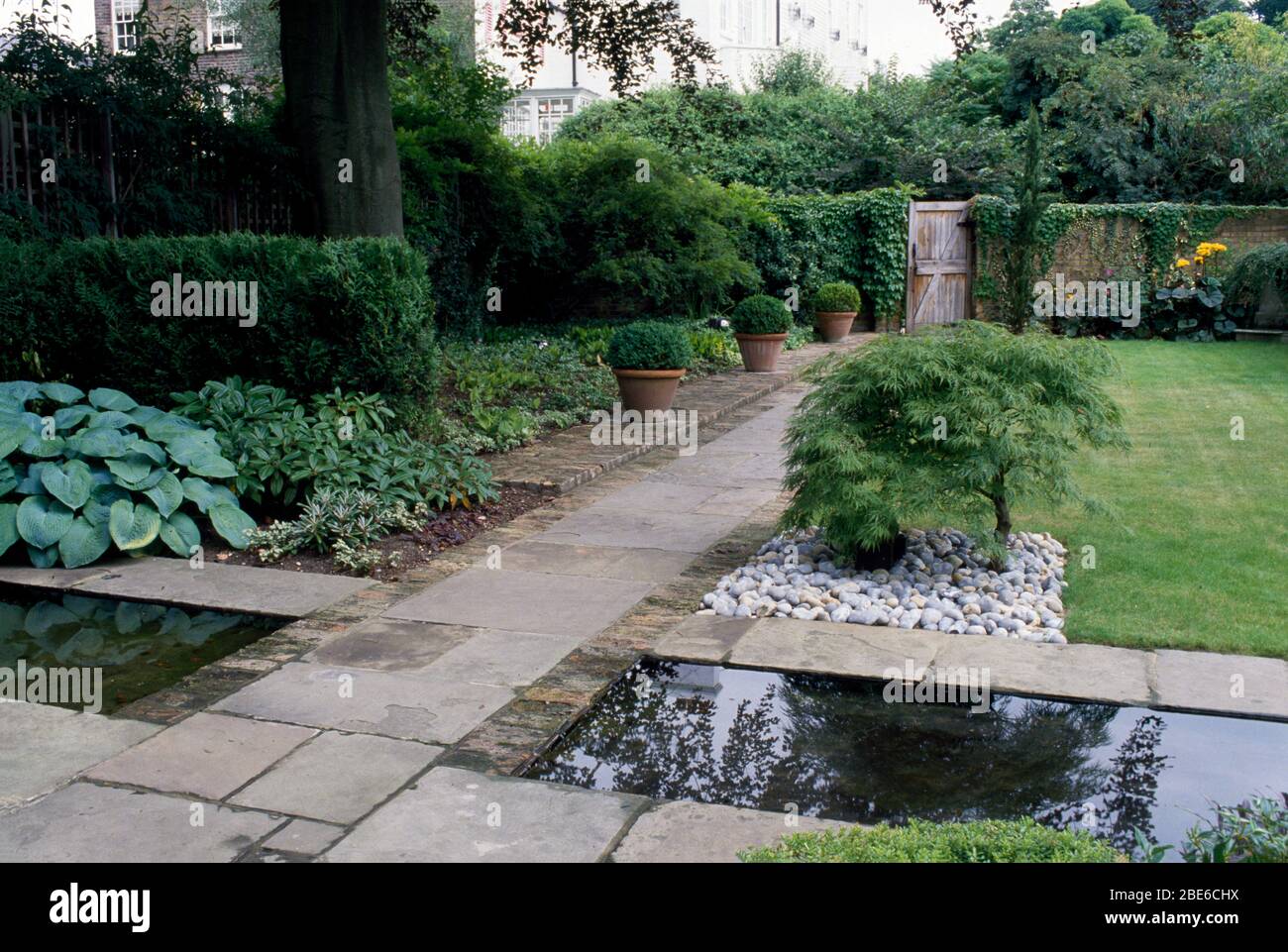 York strada in pietra su un canale a un cancello giardino con hostas, acero giapponese e palline in vaso. Foto Stock