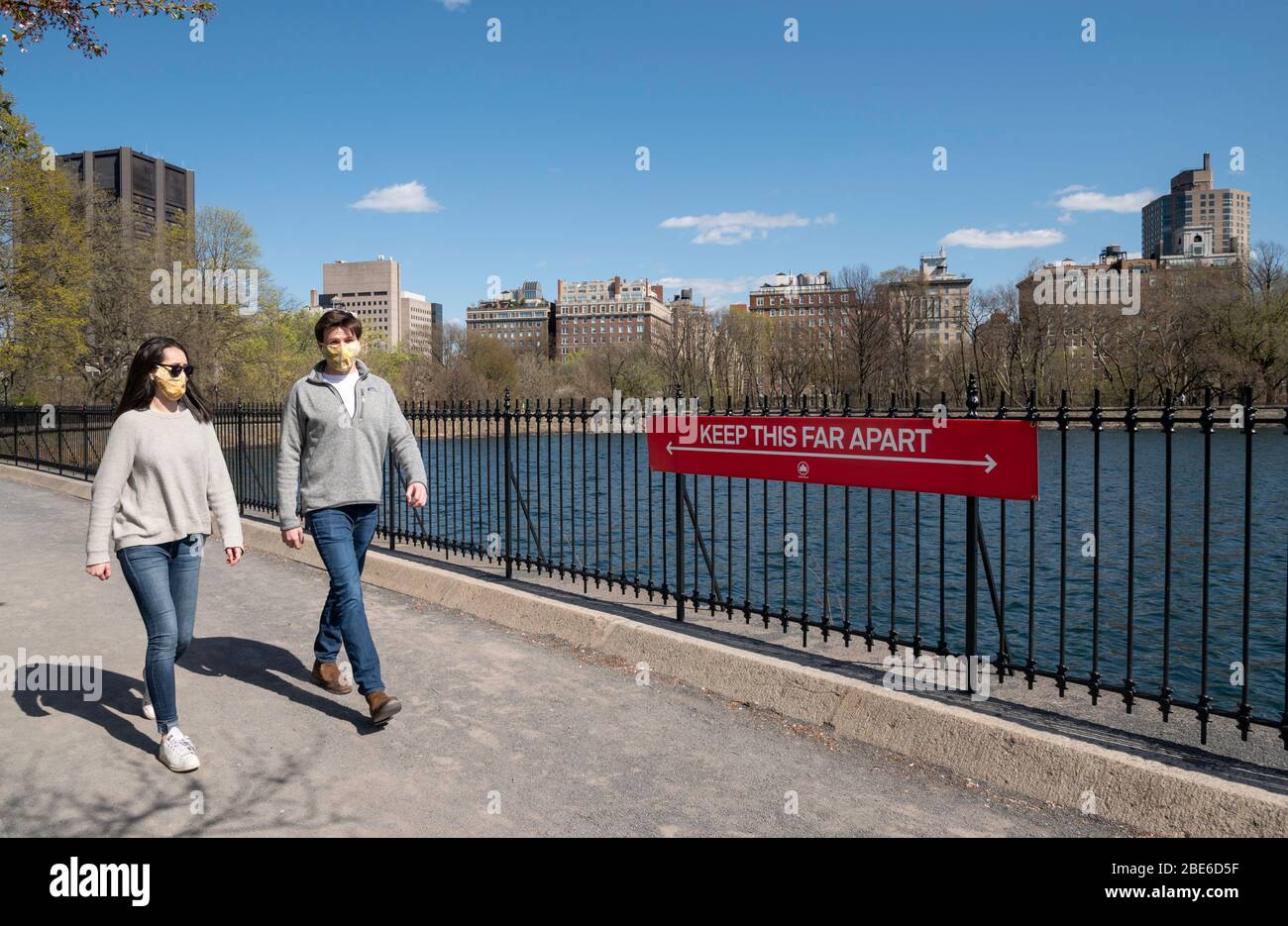 New York, NY, USA. Aprile 11, 2020. Un paio di maschere protettive cammina con un cartello sociale di distanza sulla pista di corsa al serbatoio in Central Par Foto Stock