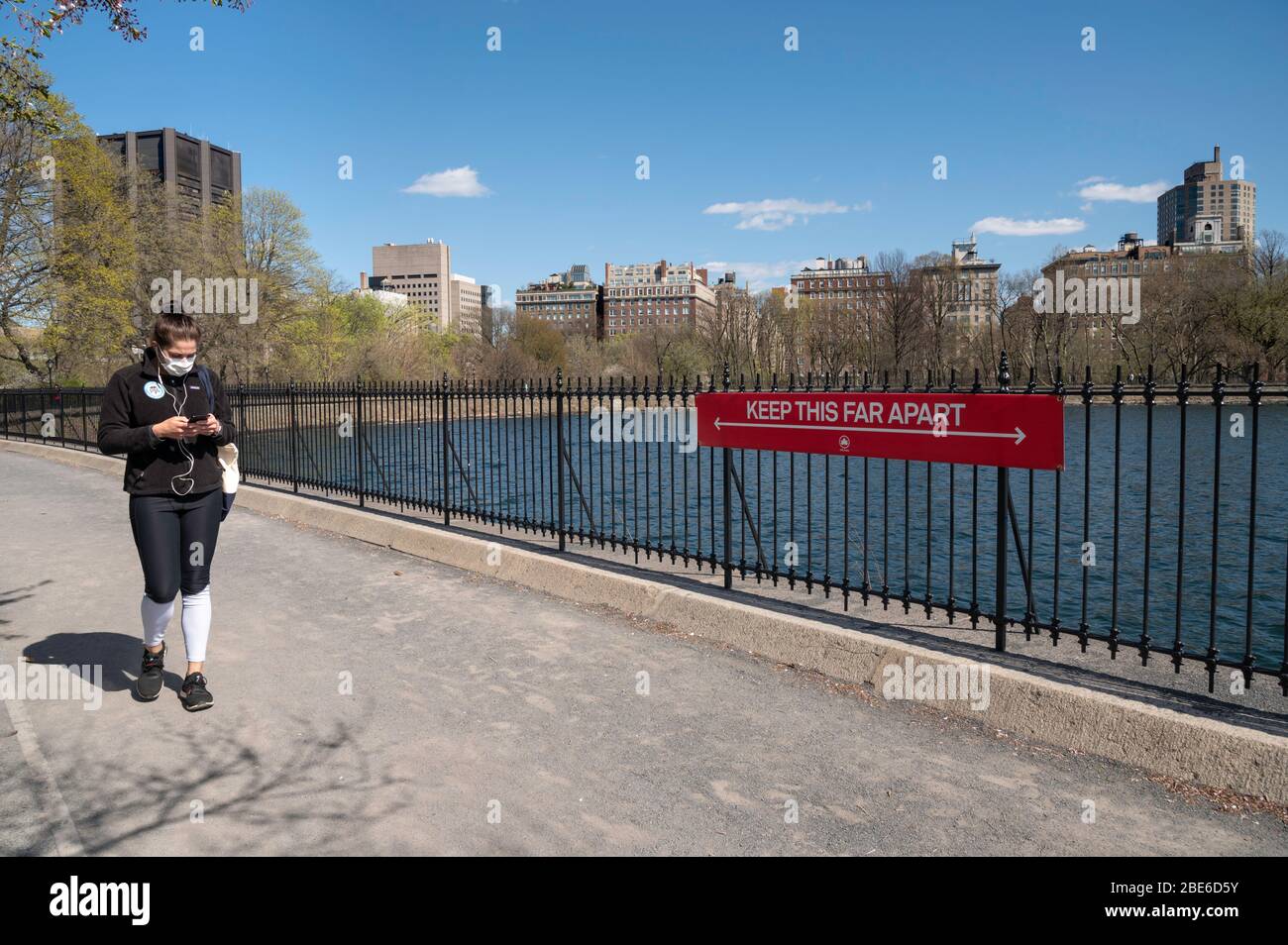 New York, NY, USA. Aprile 11, 2020. Una donna in una maschera protettiva cammina con un cartello sociale di distanza sulla pista di corsa al serbatoio in par centrale Foto Stock