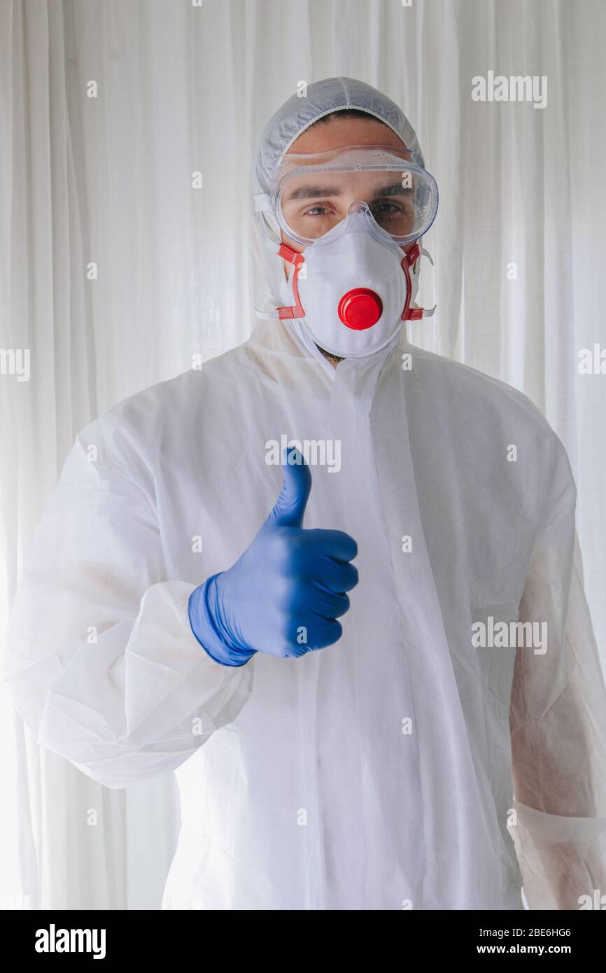 Medico in tuta protettiva e maschera facciale che solleva il pollice come un segno di approvazione Foto Stock
