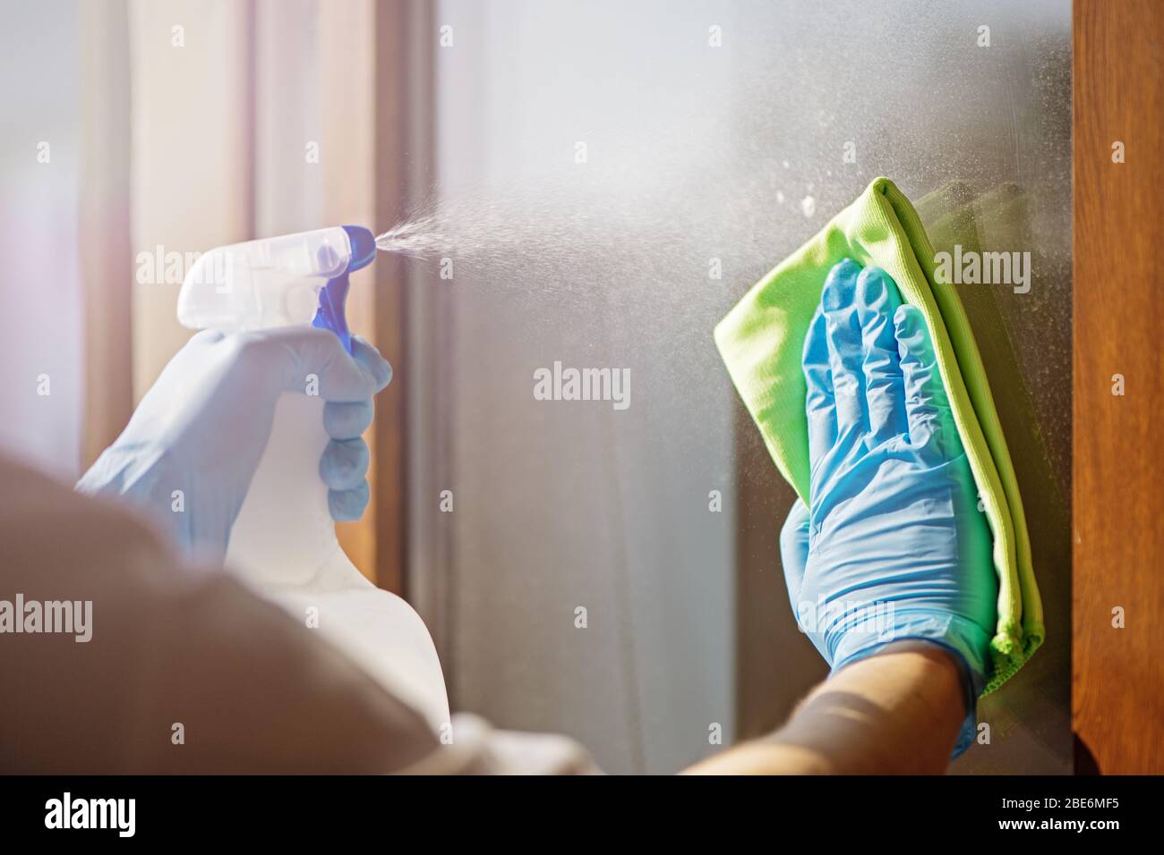 Primo piano delle mani nella finestra di pulizia dei guanti blu con straccio verde e spray. Concetto di lavoro domestico Foto Stock