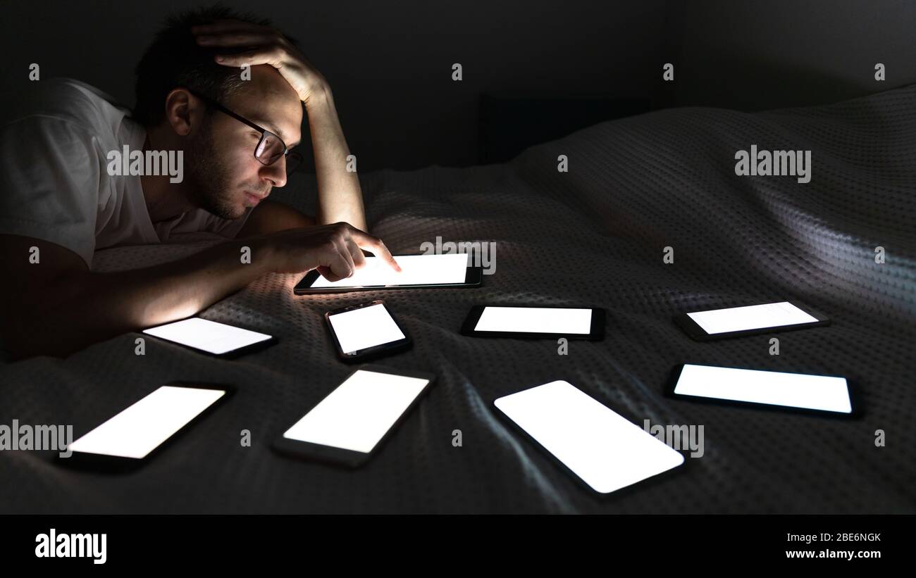 Dipendenza, nomofobia, insonnia, disturbi del sonno. L'uomo addicted del gadget usando il tablet a tarda notte, chiacchierando sui social network, disteso nel letto intorno a. Foto Stock