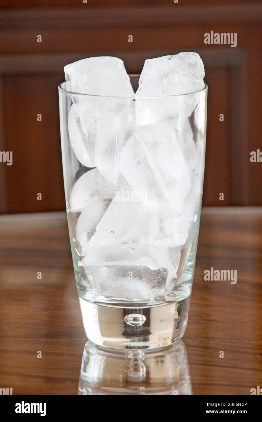 Pezzi di ghiaccio che riempiono un bicchiere su uno sfondo scuro Foto Stock